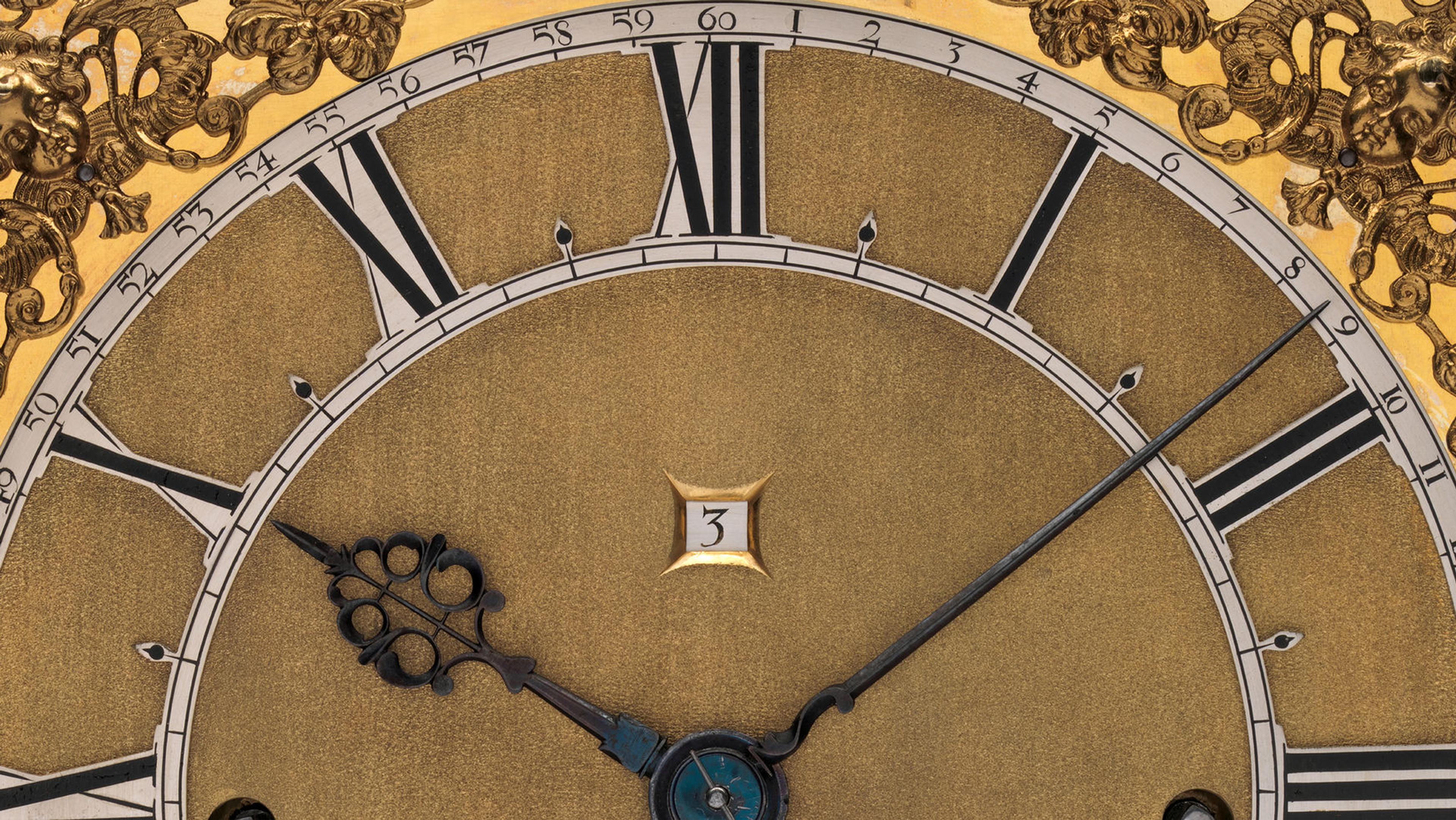 Detail of a clock face with gold-colored accents, roman numeral numbers, and a counter for the date.