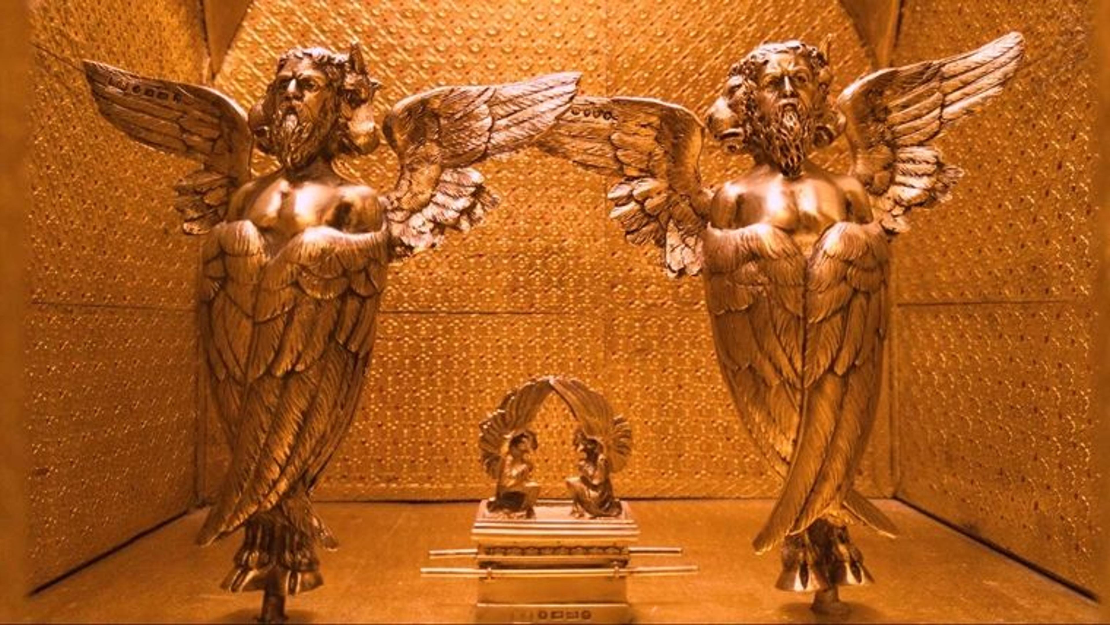 A golden model room with two gold statues of ancient angels and an ornate cabinet between them.