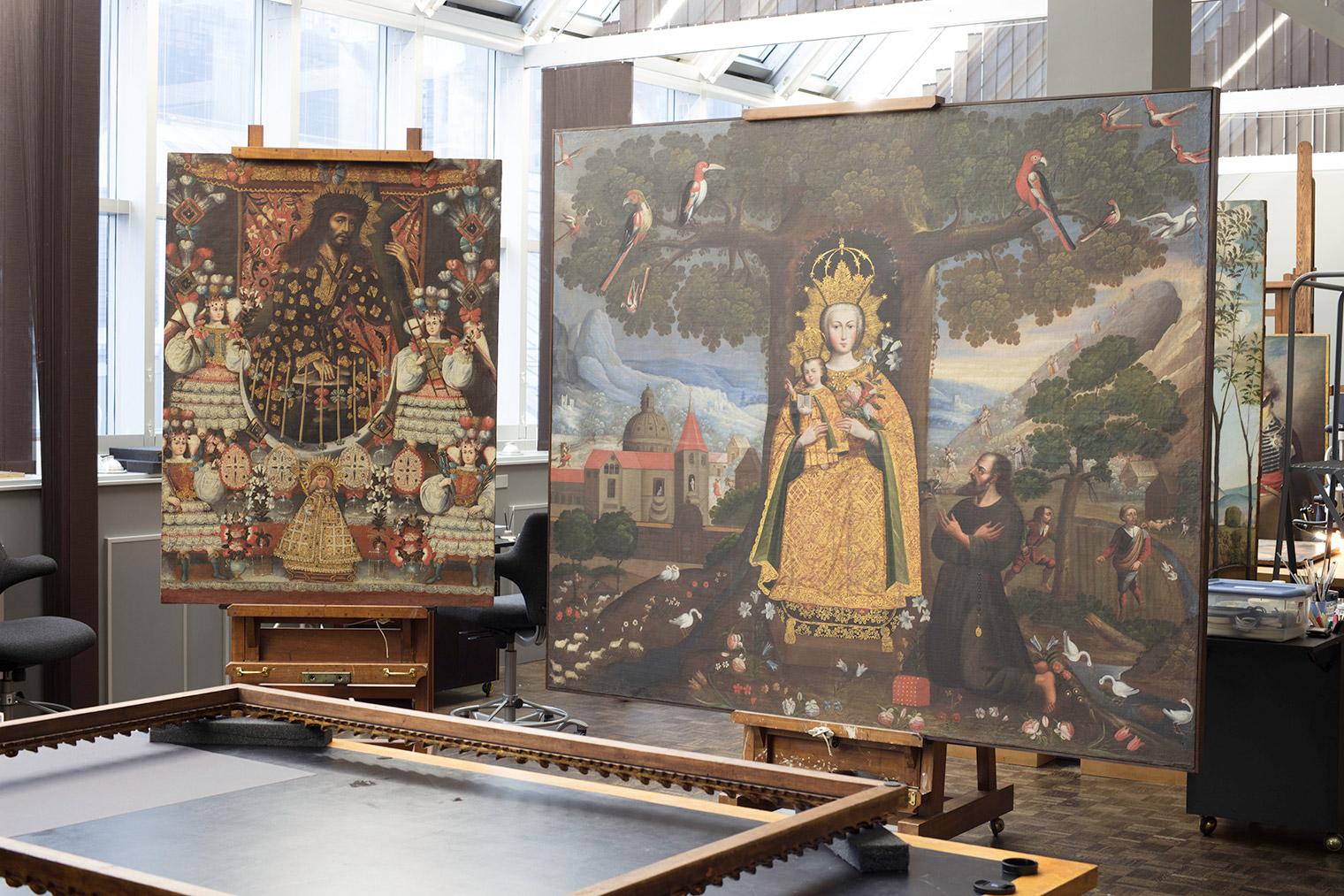 Photograph of two paintings perched on easels within a sunlight-filled conservation studio