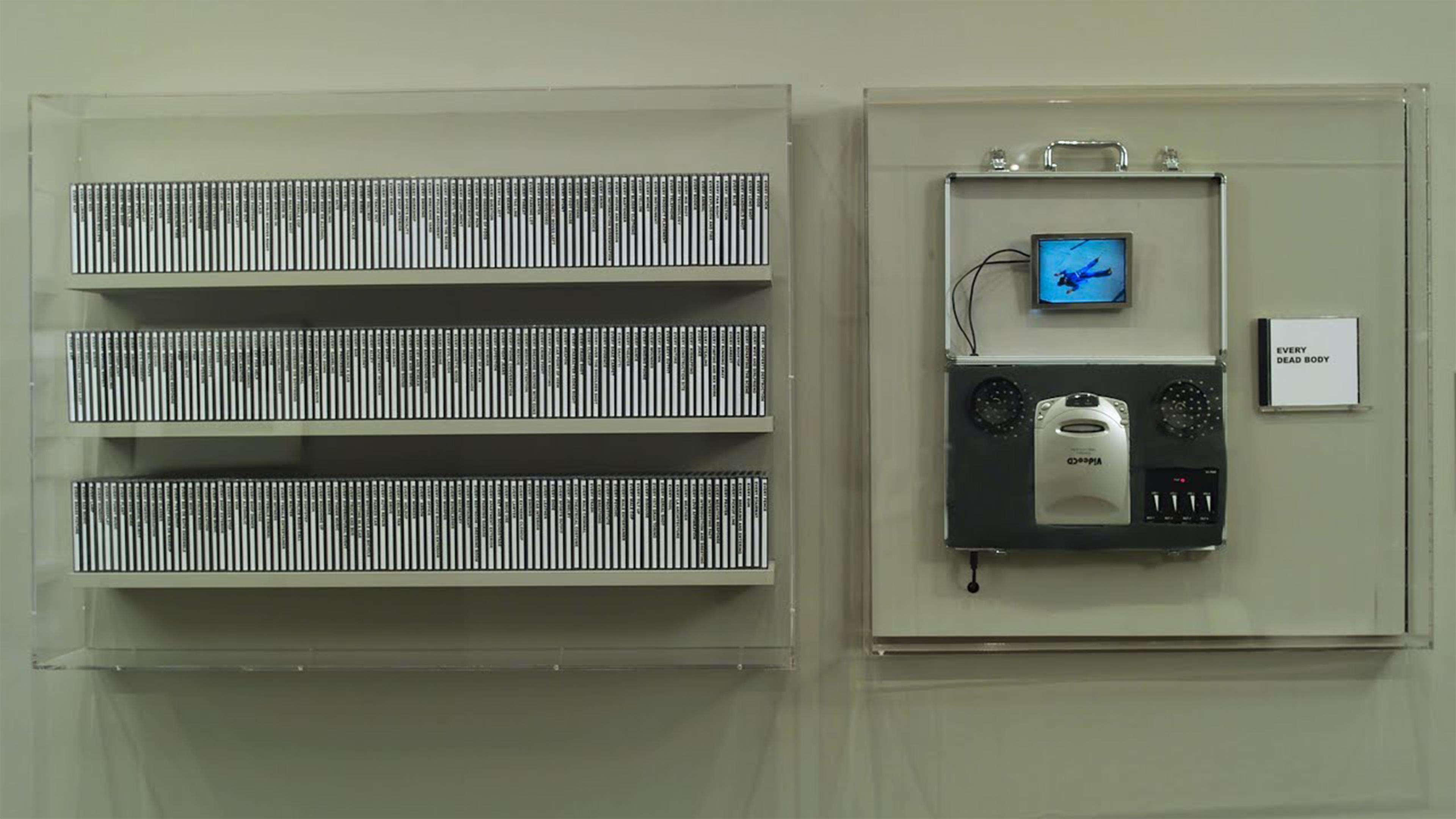 A wall display features rows of neatly arranged cassettes on the left and a multimedia installation on the right, including a small screen and speakers.
