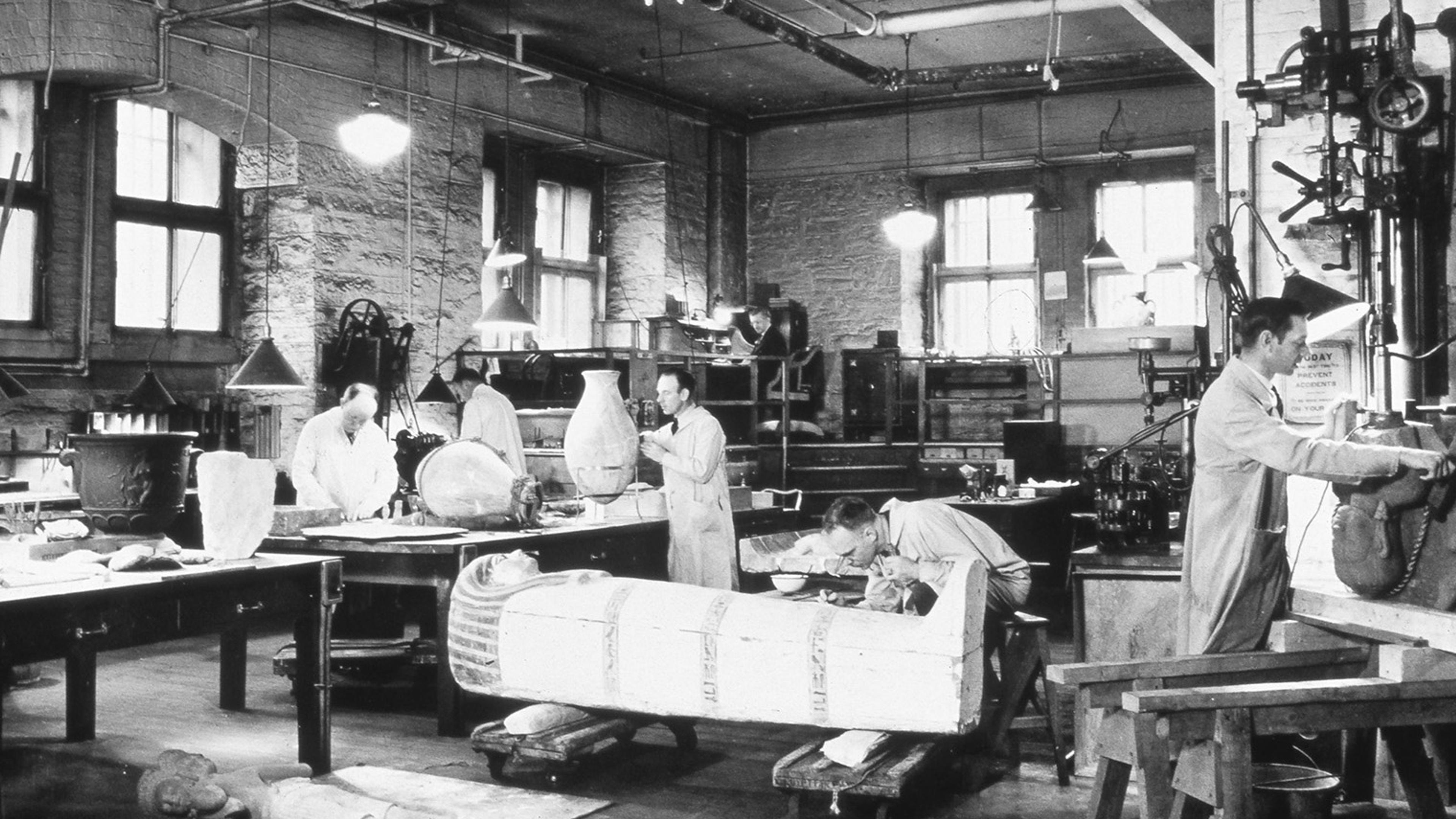 A black and white photograph from November 4, 1936, of four conservators at work on various objects, including an anthropoid coffin of Harmose (36.3.172).