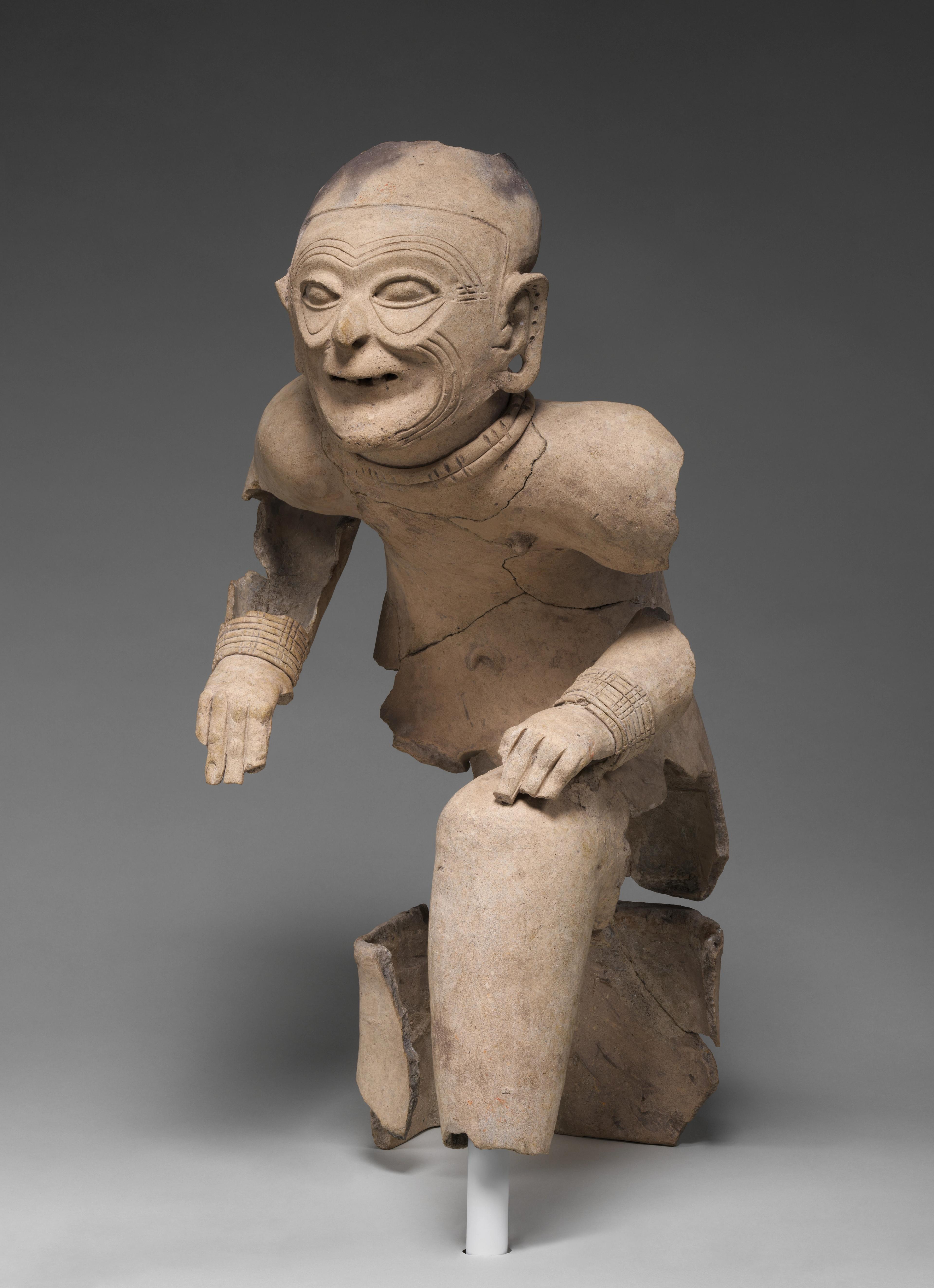 Ceramic statue of an elder with facial wrinkles seated in a crouched position.