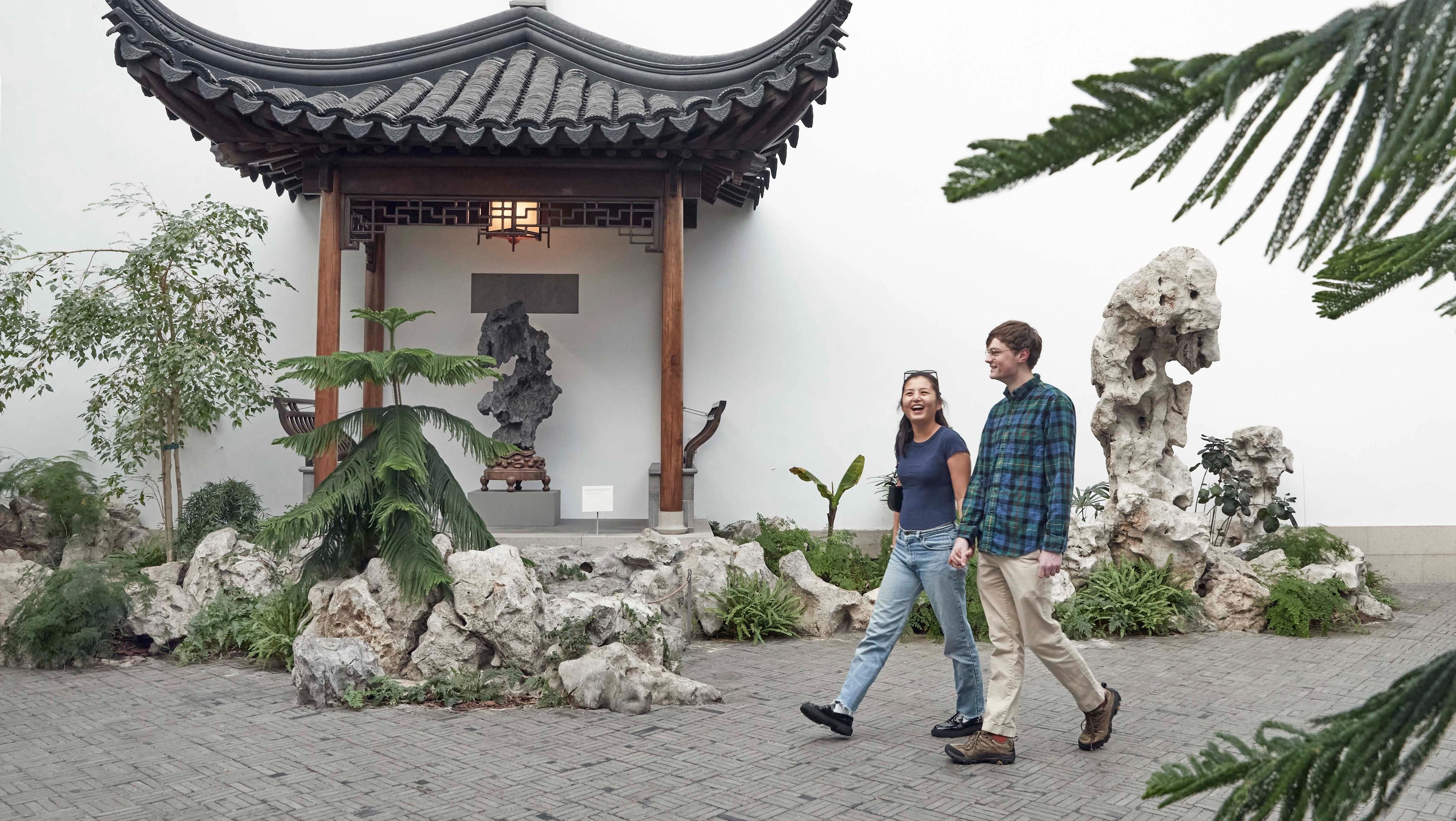 A man and woman walking in The Met's Astor Court.
