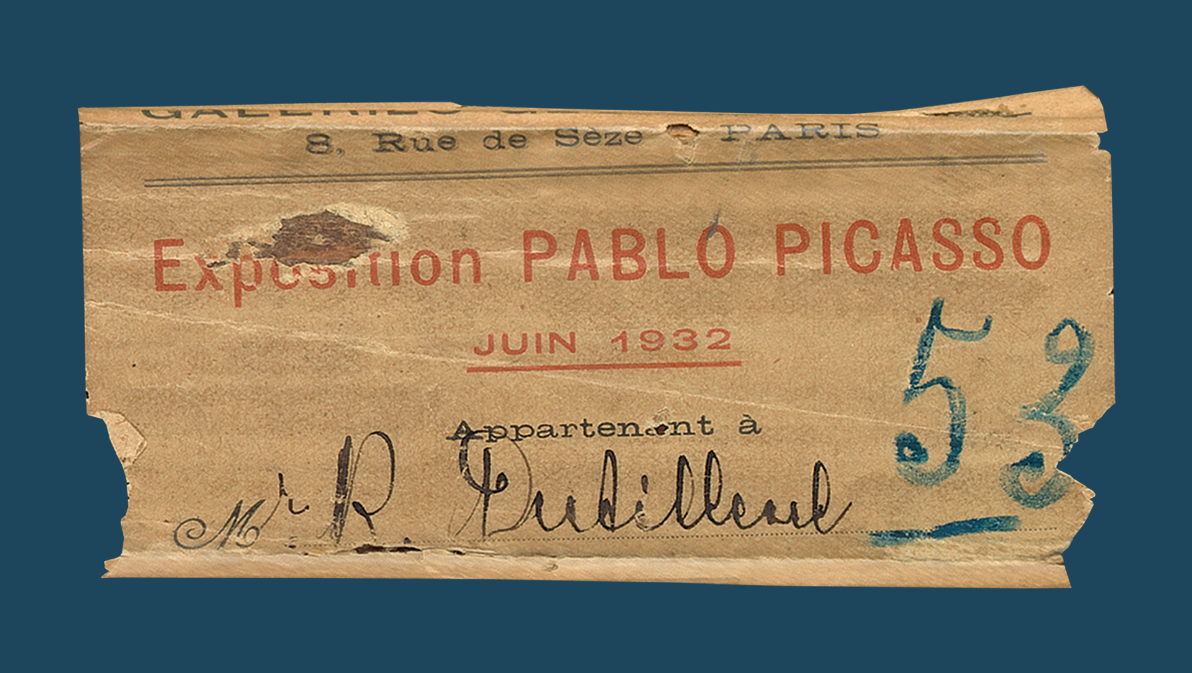 Torn label with "Exposition Pablo Picasso" typed in red and 53 written in blue on a blue background