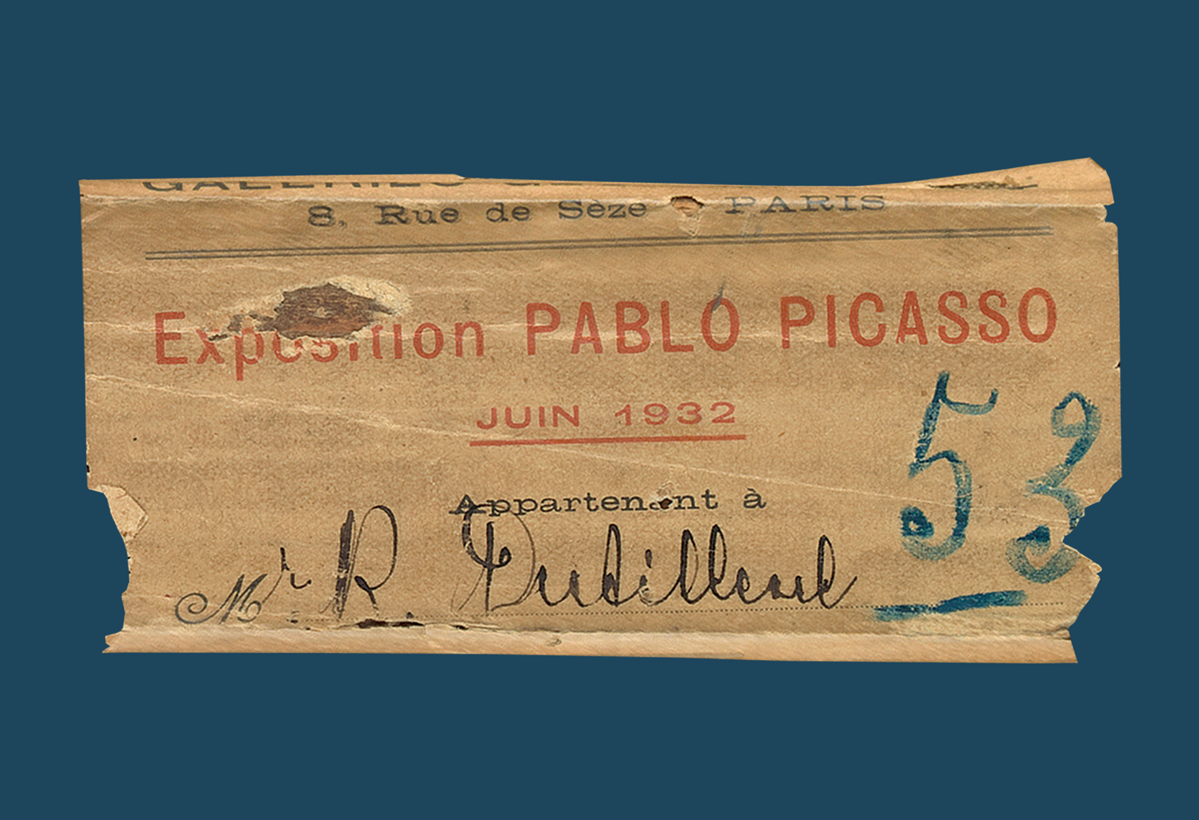 Torn label with "Exposition Pablo Picasso" typed in red and 53 written in blue on a blue background