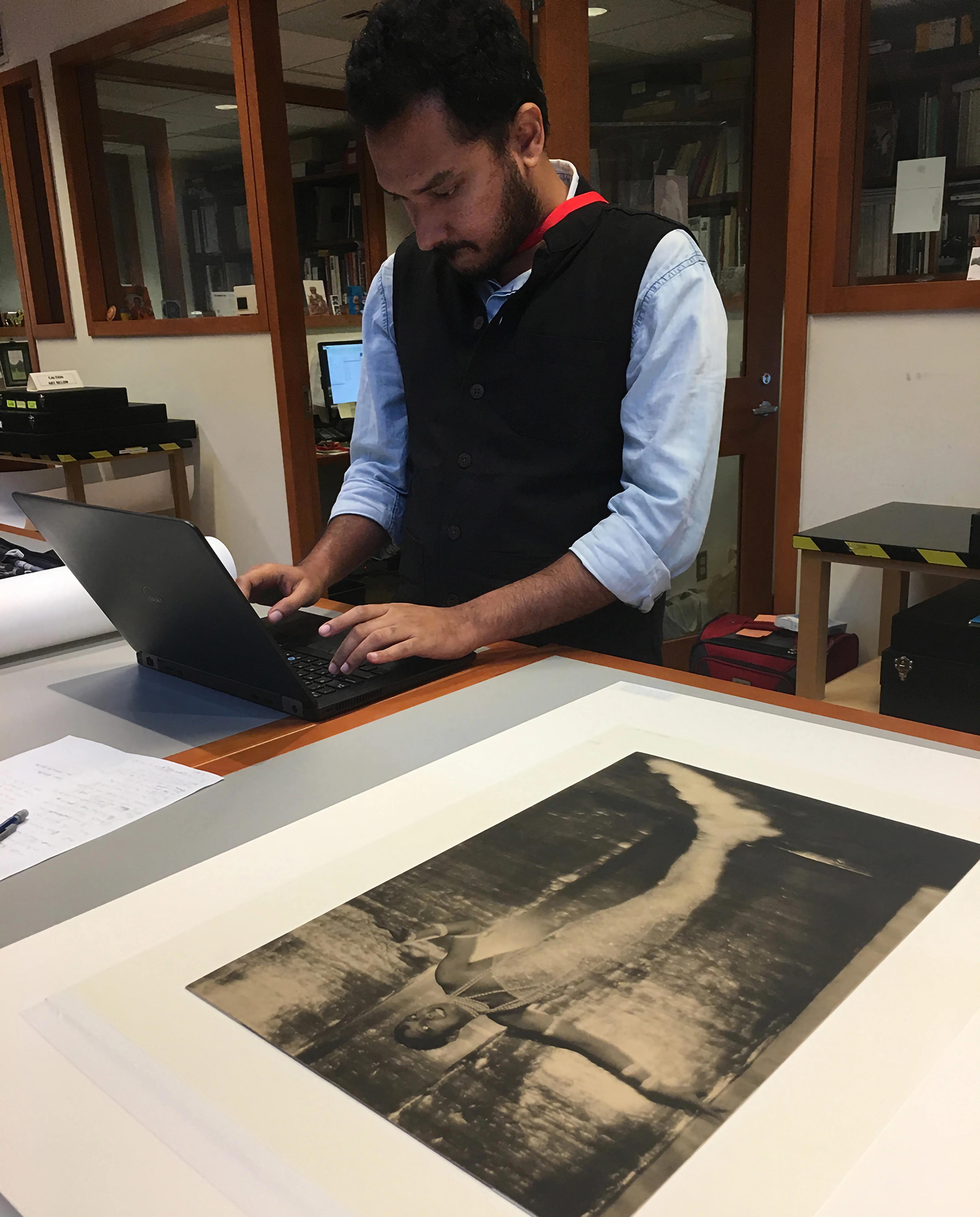 A person working on a laptop, which is placed on a table next to a printed photograph of Josephine Baker.