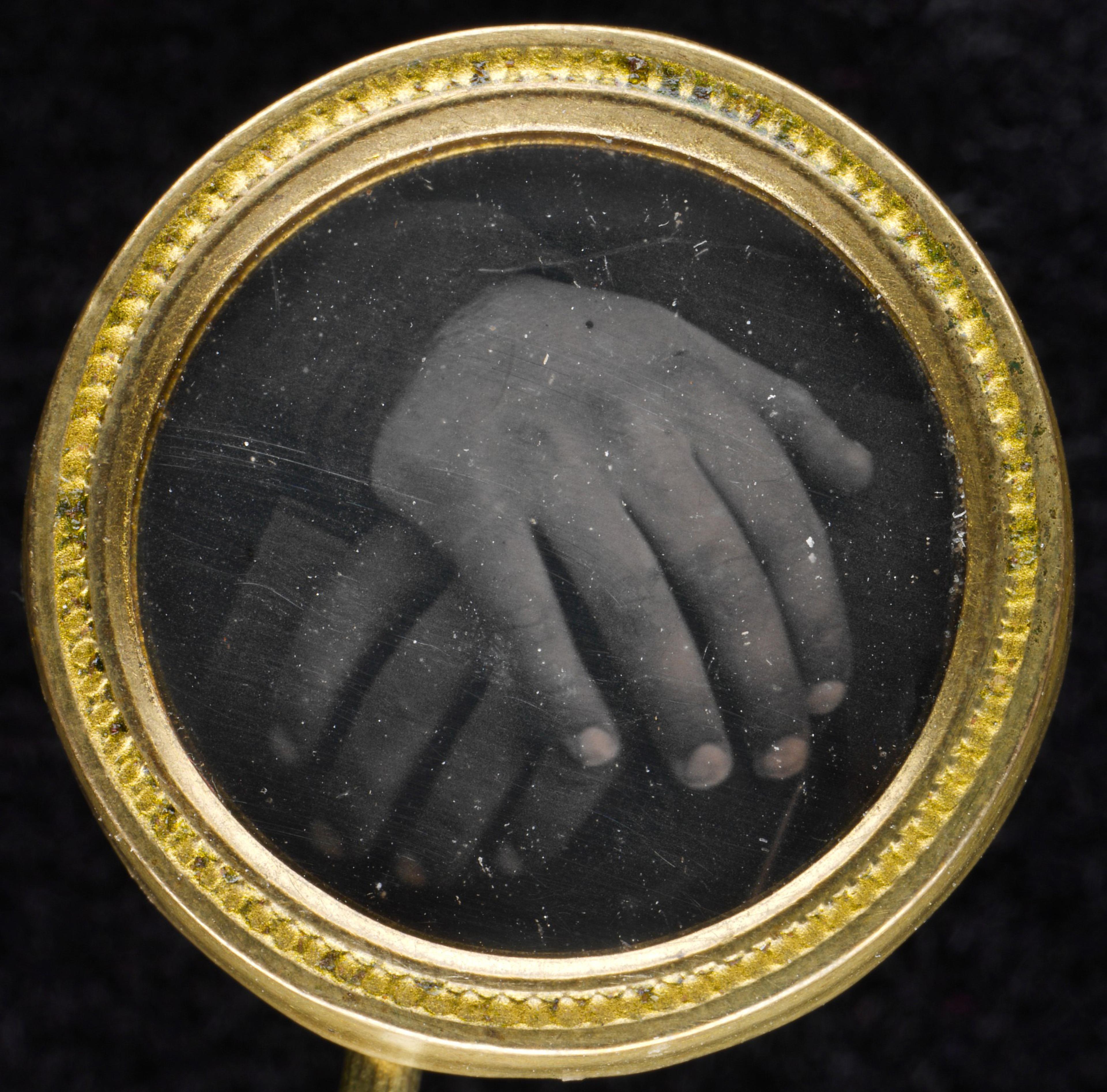 Circular gold button framing a black and white photograph of two hands.