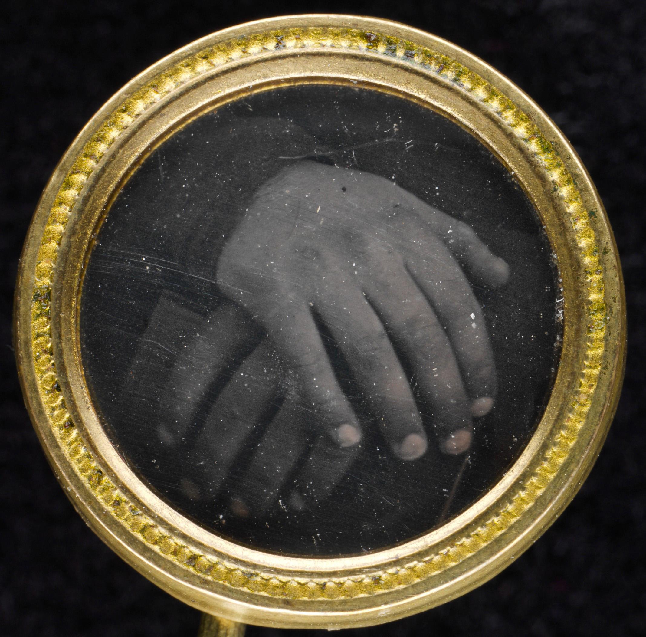 Circular gold button framing a black and white photograph of two hands.