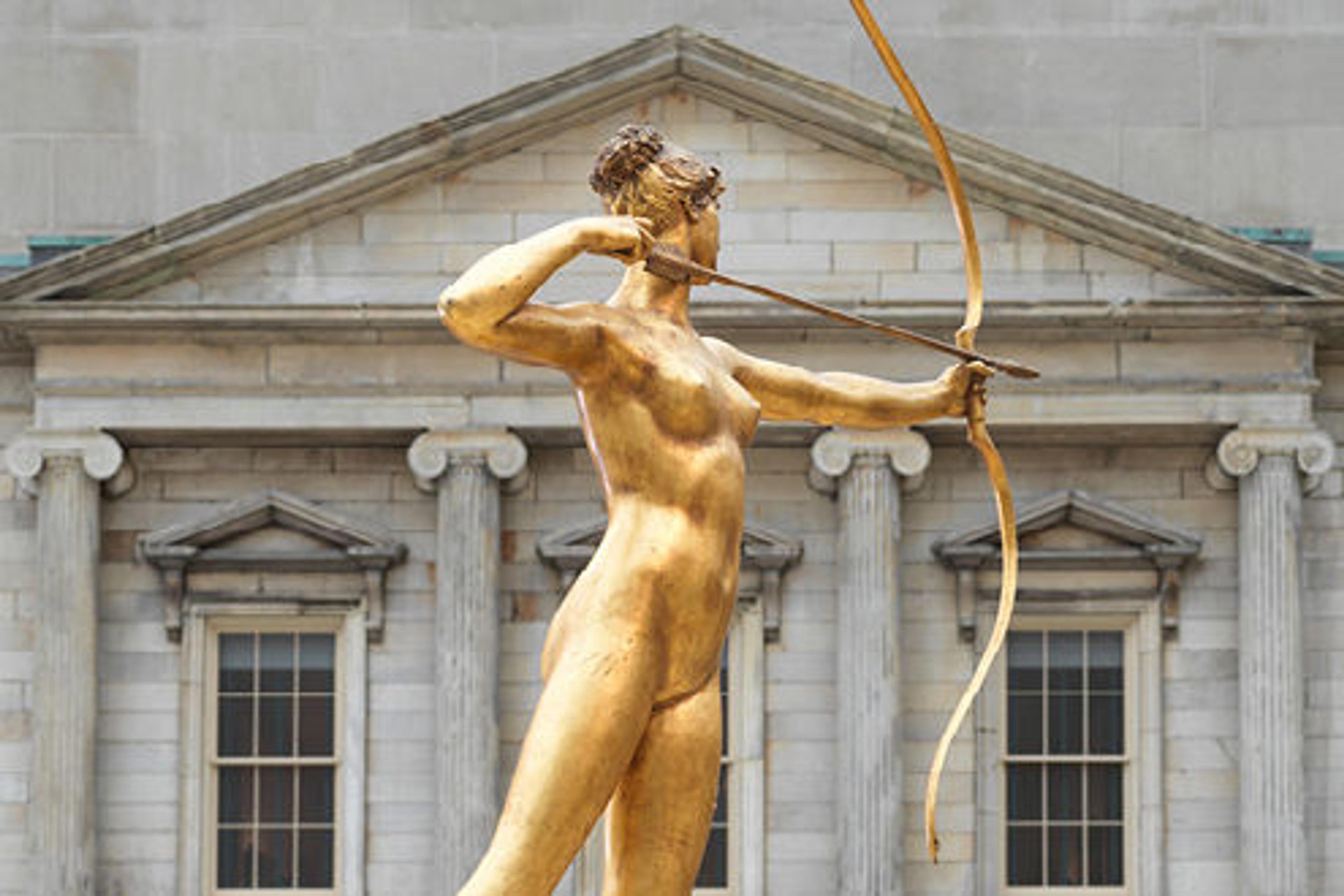 A statue of a woman wielding a bow and arrow with a building facade with large columns behind.