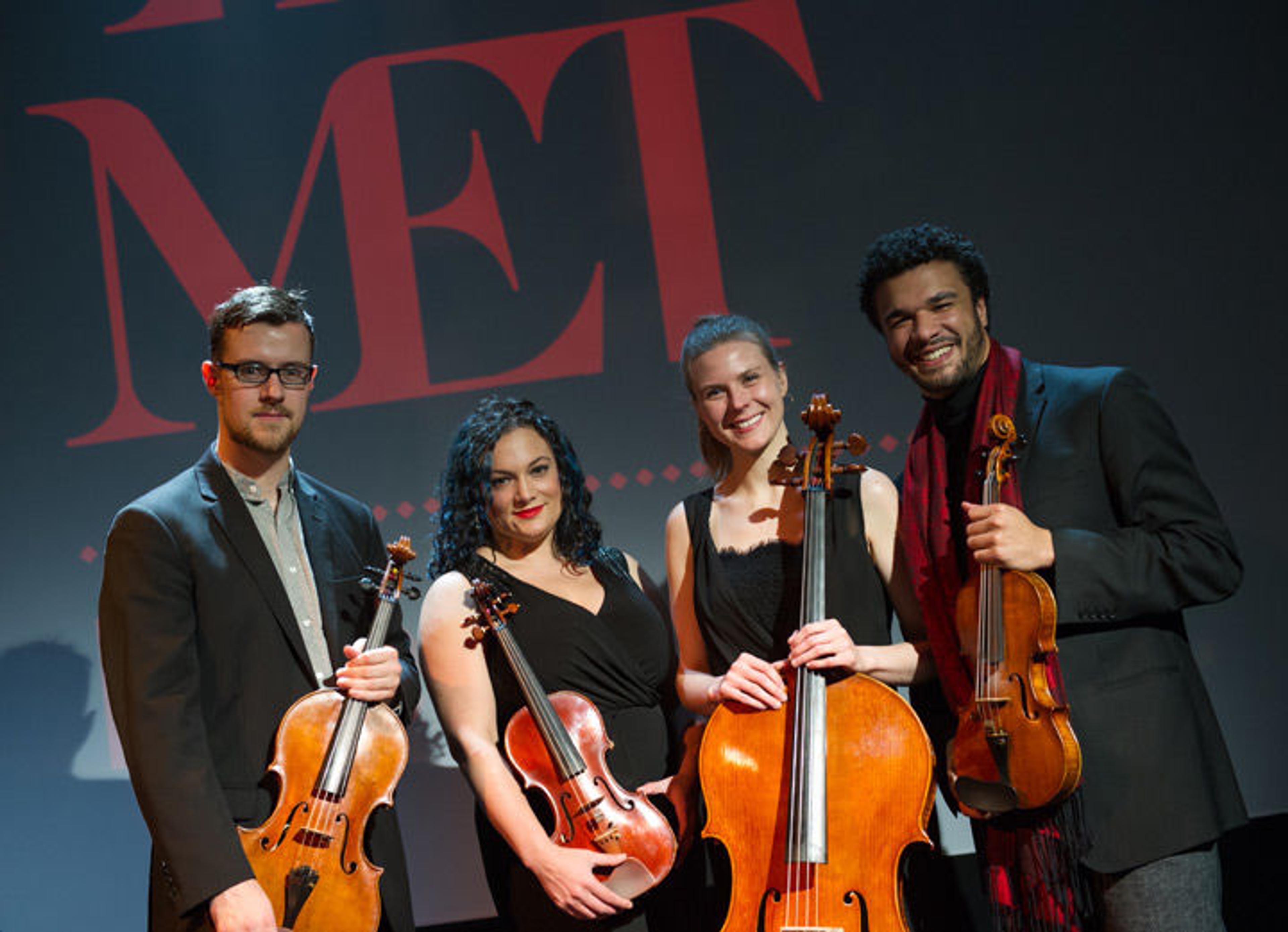 PUBLIQuartet pose in front of The Met's logo holding their instruments