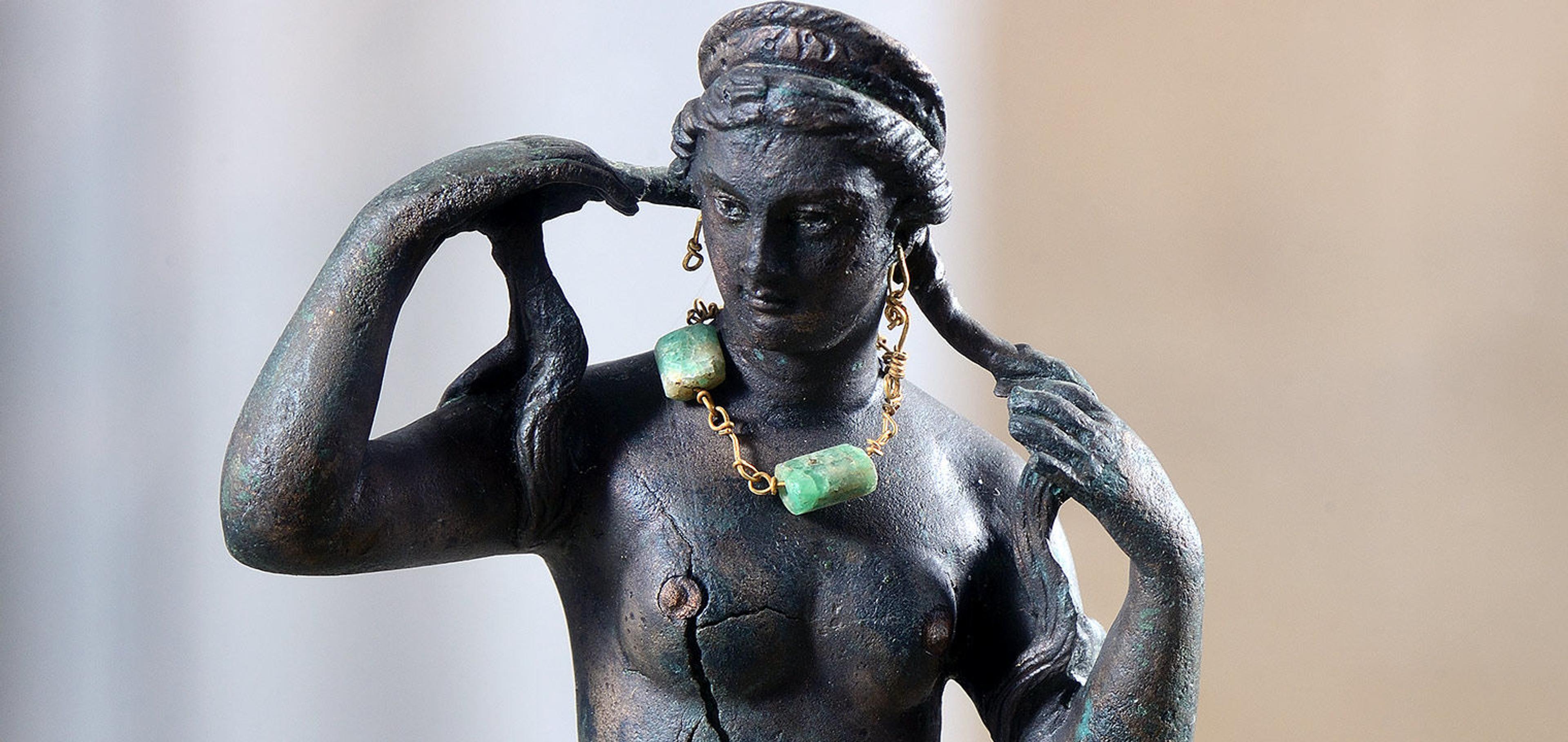 Detail of Aphrodite figurine holding her wet braids in her hands and wearing a green emerald necklace