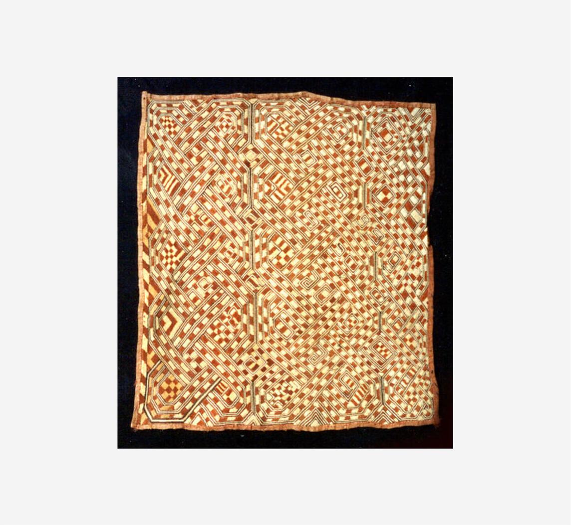 Woven textile with an intricate grid of interlocking geometric patterns in brown, cream, and reddish tones.