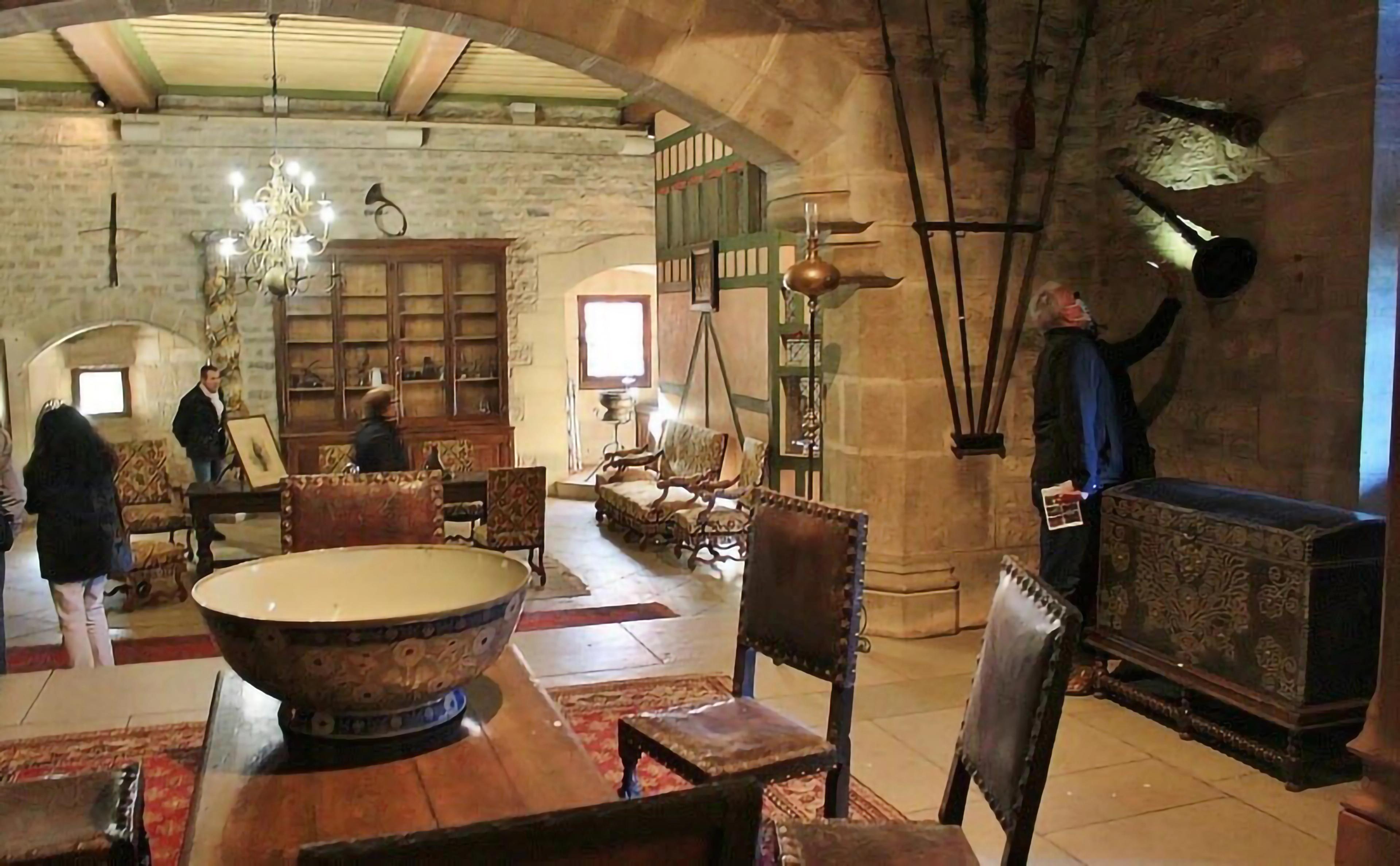 A room with arched stone beams, with people milling about and inspecting the antique furniture