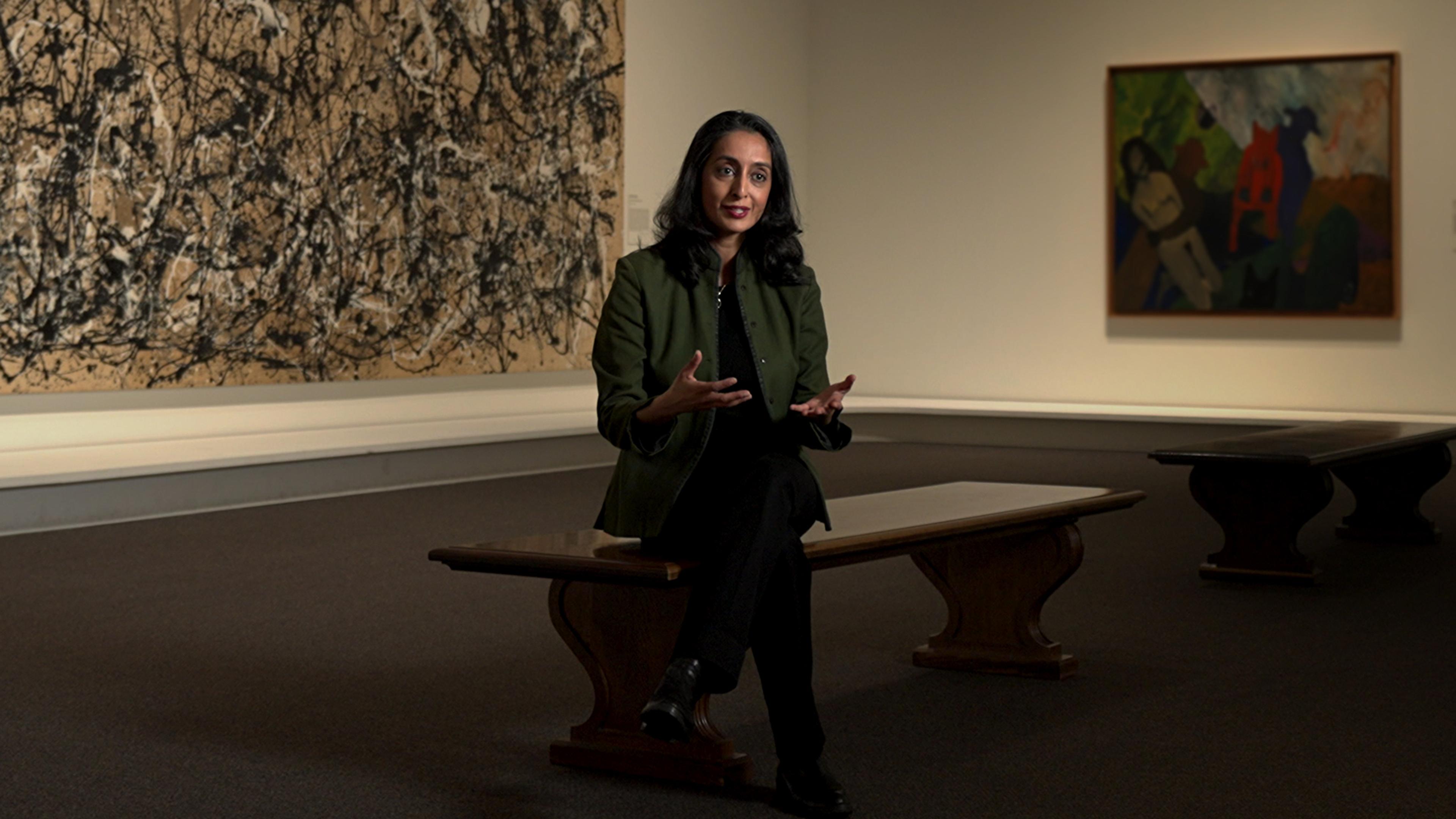 Woman seated on a bench in a museum gallery in front of a large abstract painting.
