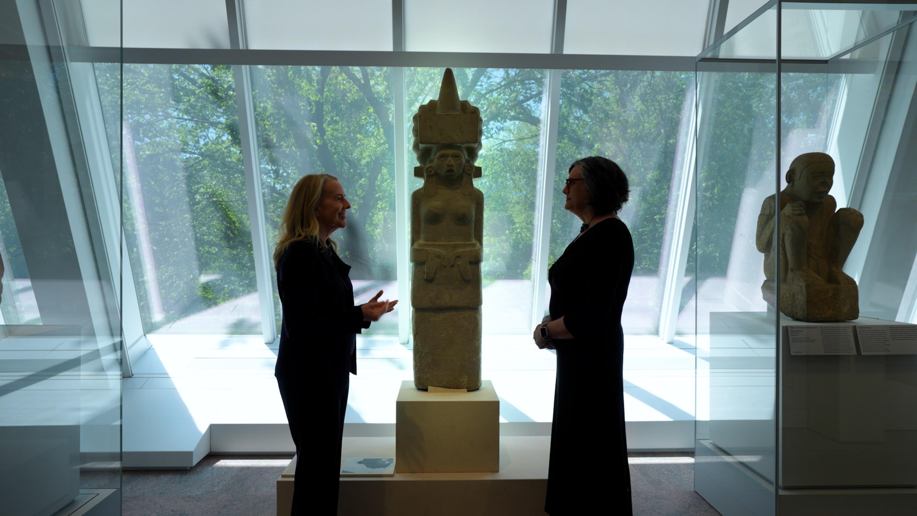 Joanne Pillsbury and Laura Filloy Nadal standing in front of a female sculpture in the Ancient Americas galleries of the Michael C. Rockefeller Wing