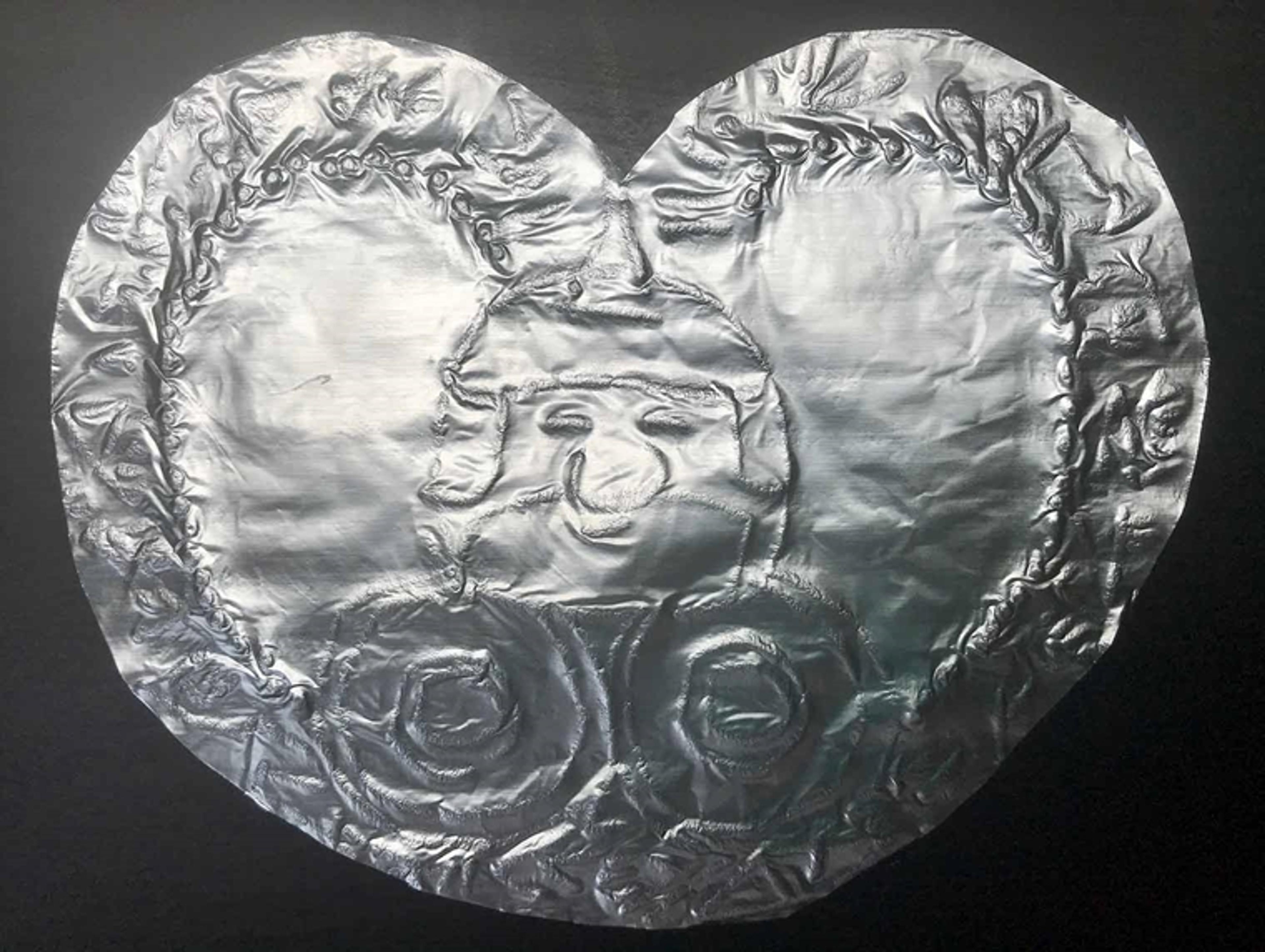A heart-shaped tin foil ornament with a face of a man in the center with two circles below it.