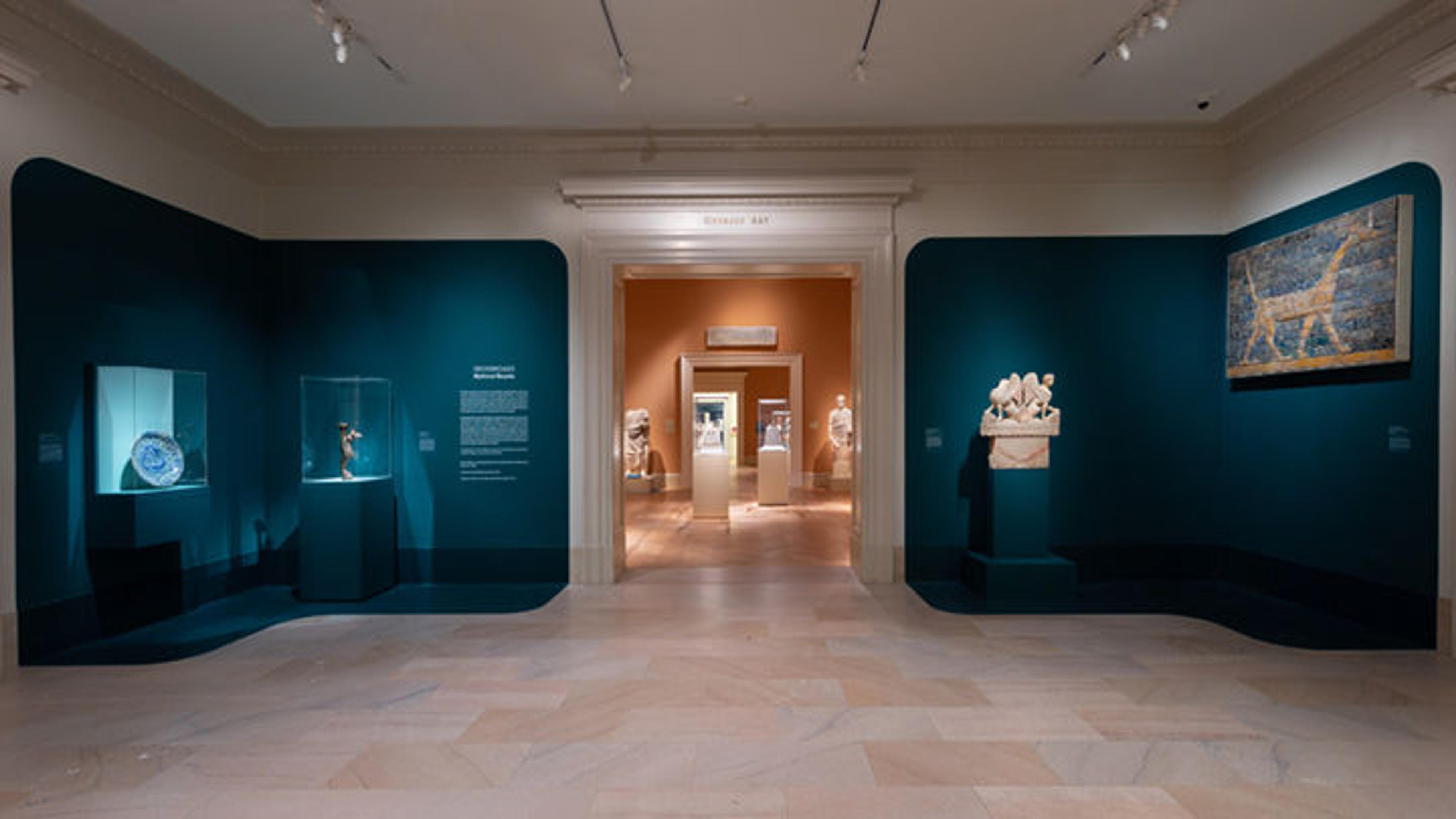 A view of a blue gallery with four objects hung on the walls