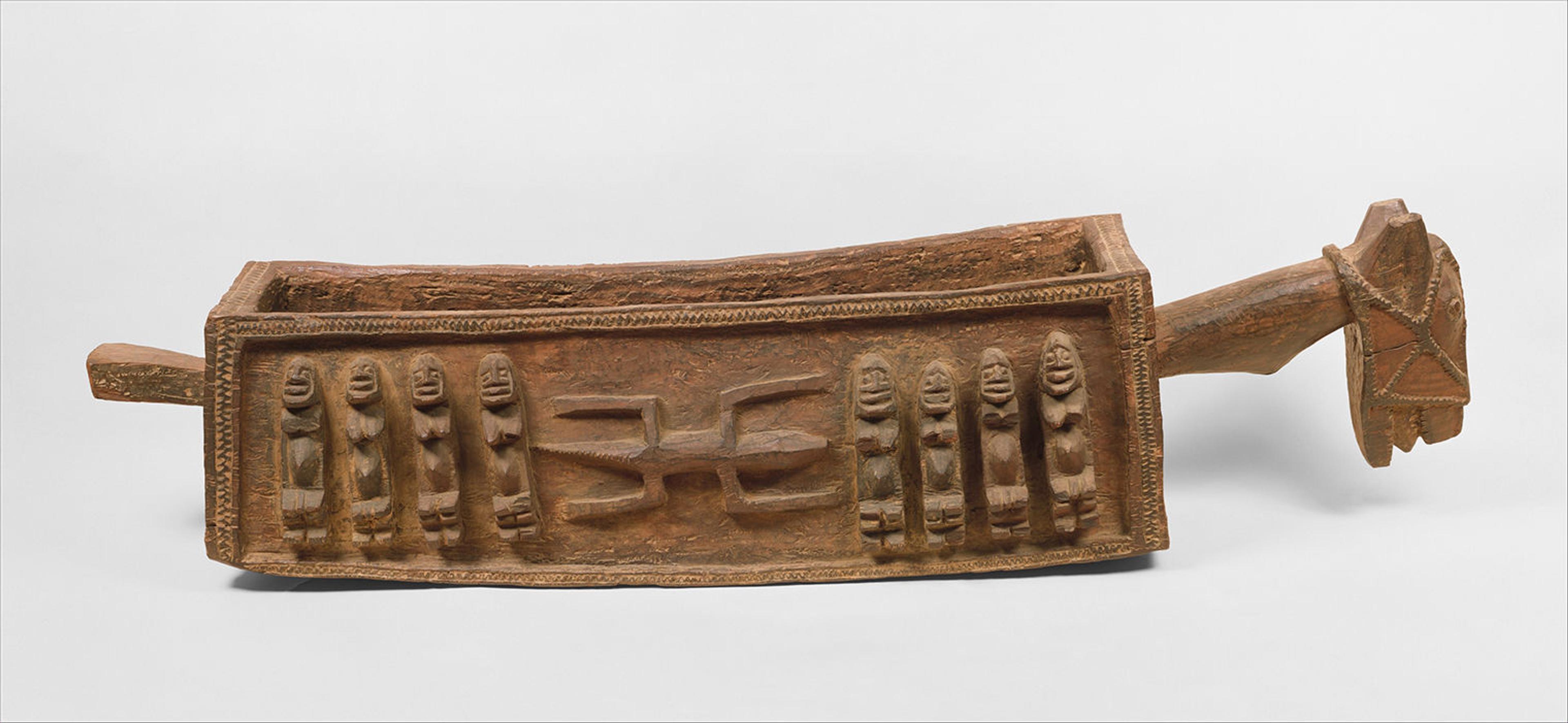 Picture of a ritual vessel. It's hollow on the inside, made of wood, and has figures and designs carved into its surface.