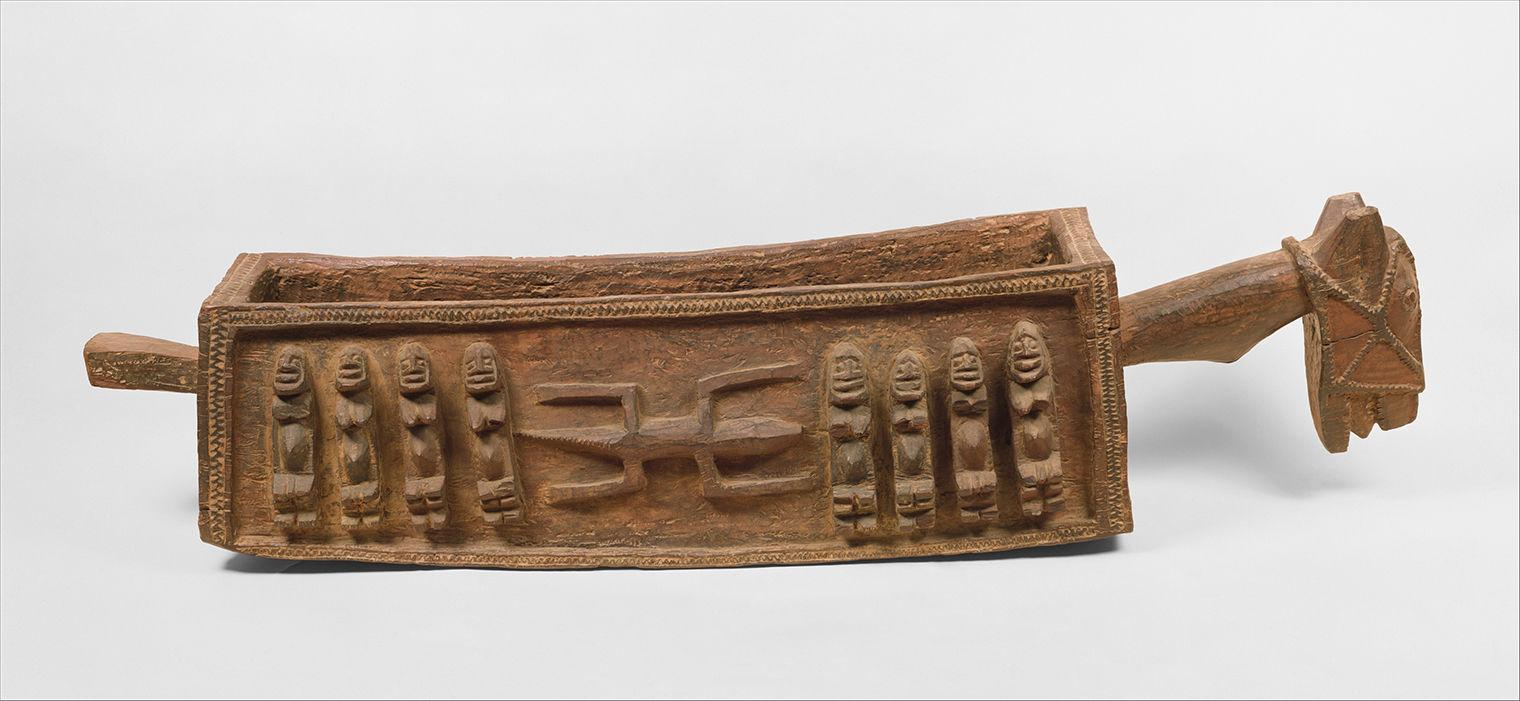 Picture of a ritual vessel. It's hollow on the inside, made of wood, and has figures and designs carved into its surface.