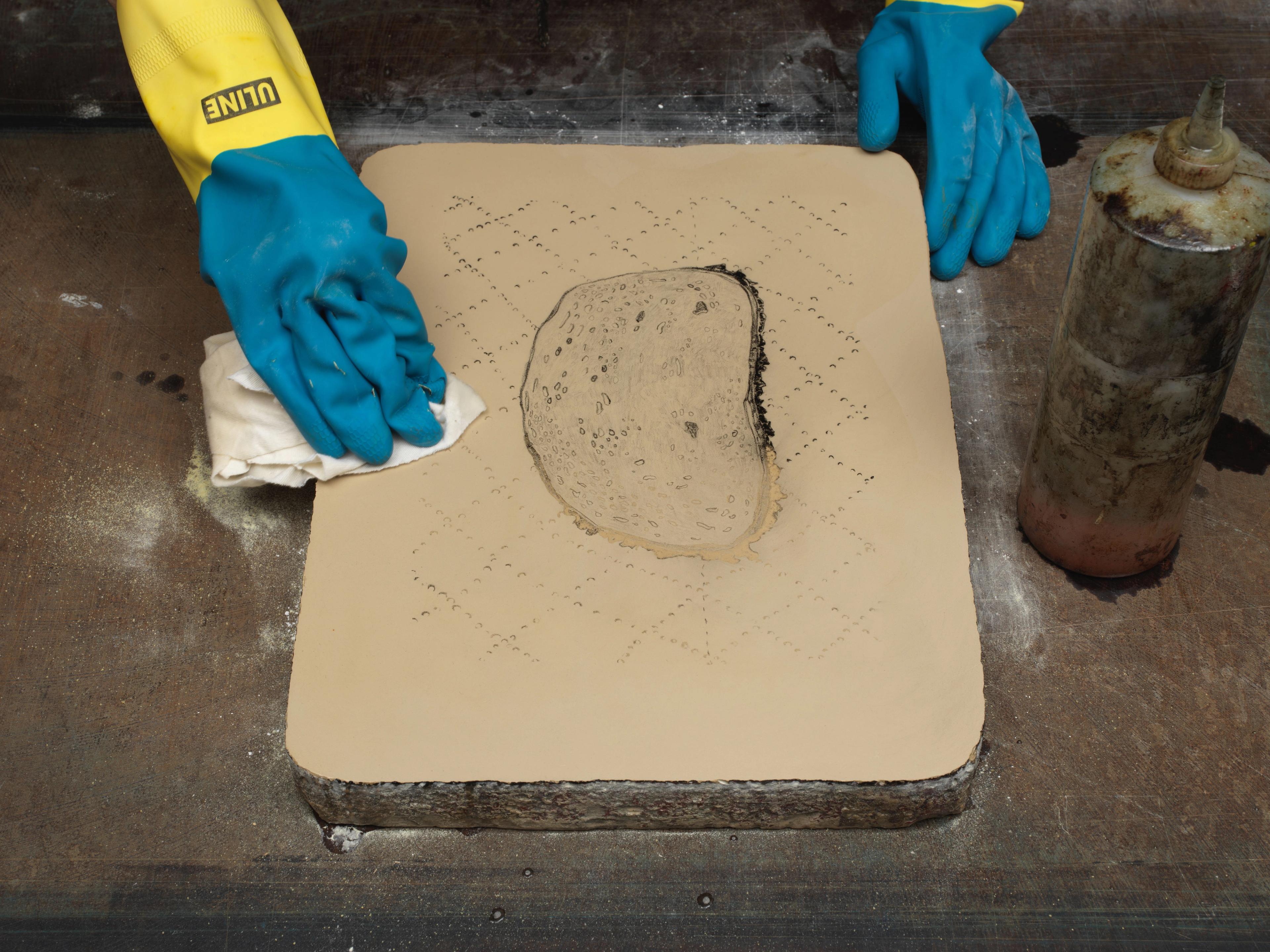 Photograph of an artists hands wearing gloves, dissolving a lithography drawing with solvent.