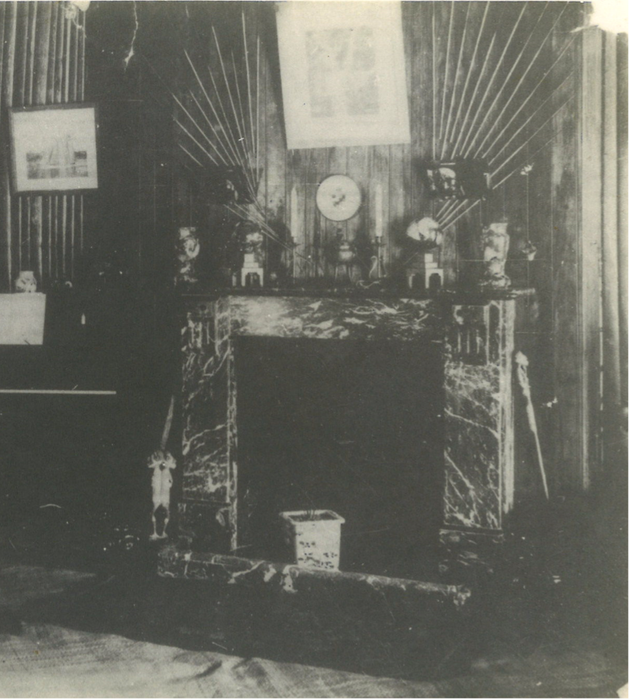 Fireplace with an oversized spatula leaning against it and a freestanding carving of two figures standing back-to-back on the ground nearby.