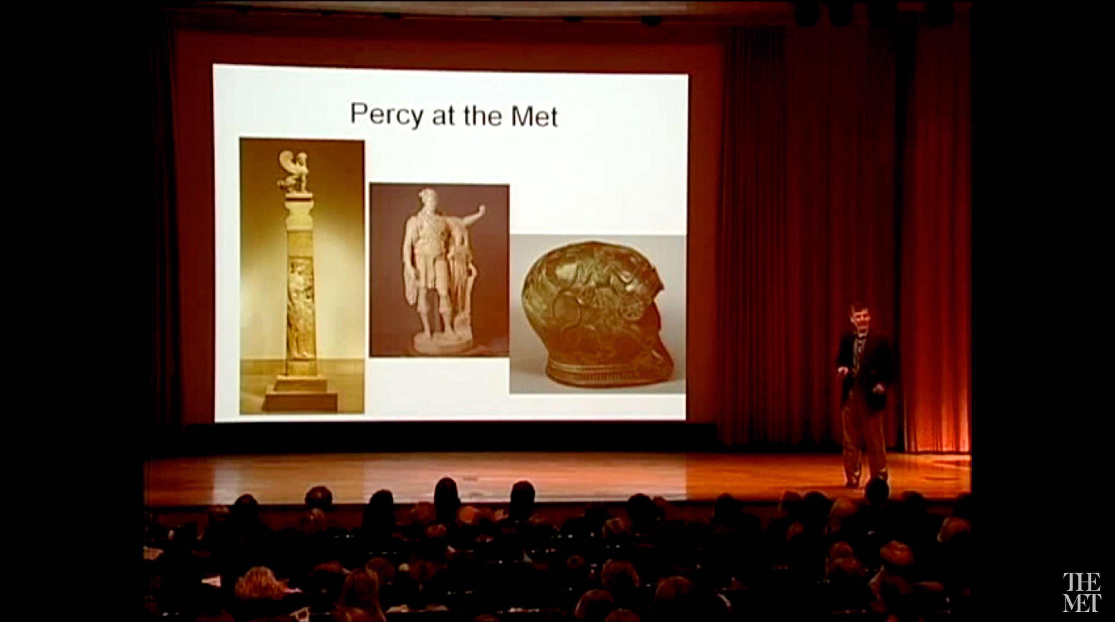 A screen in a lecture hall displaying three Greek and Roman artworks