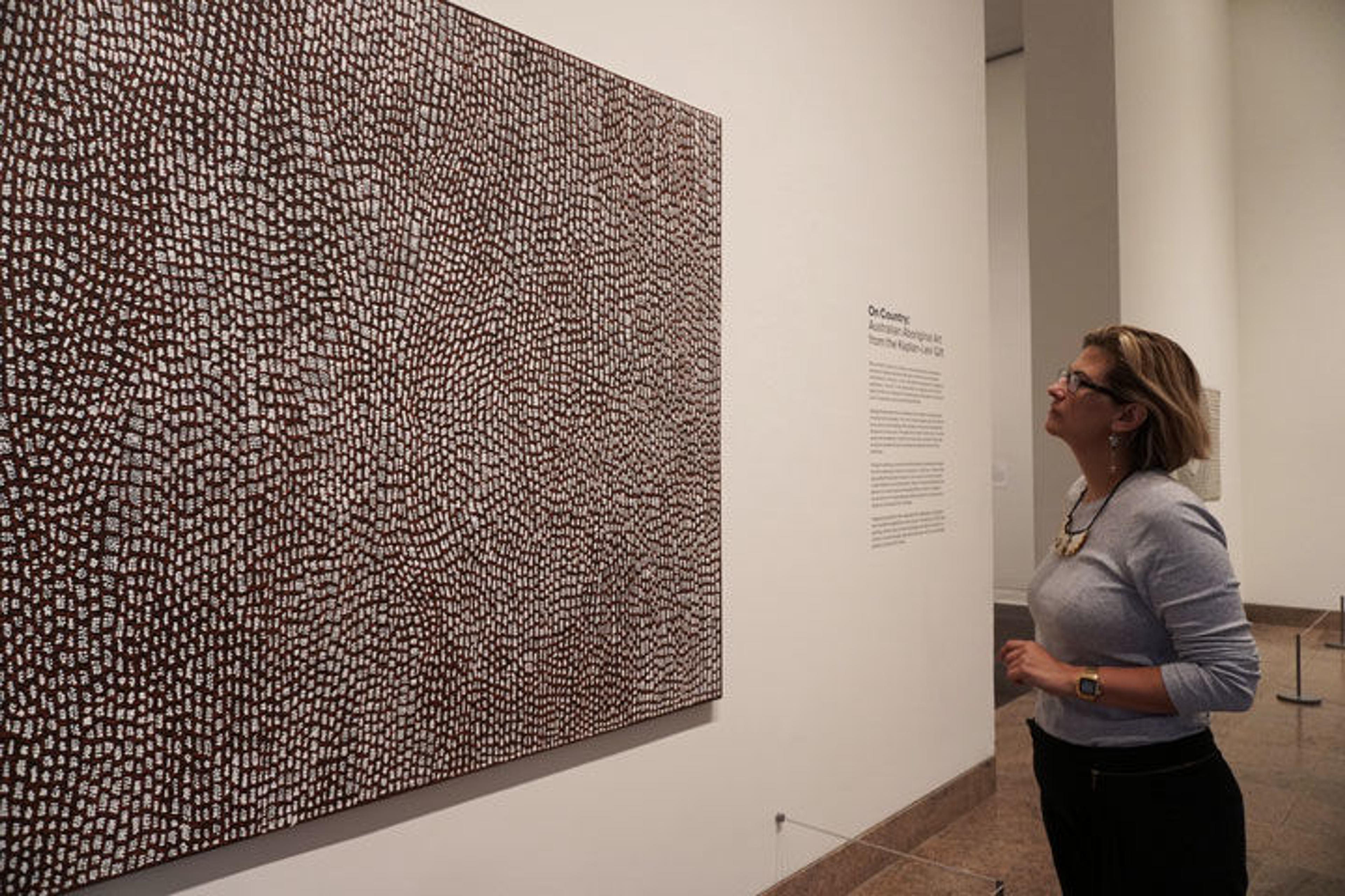Associate Curator Maia Nuku observes a painting on view in an exhibition gallery