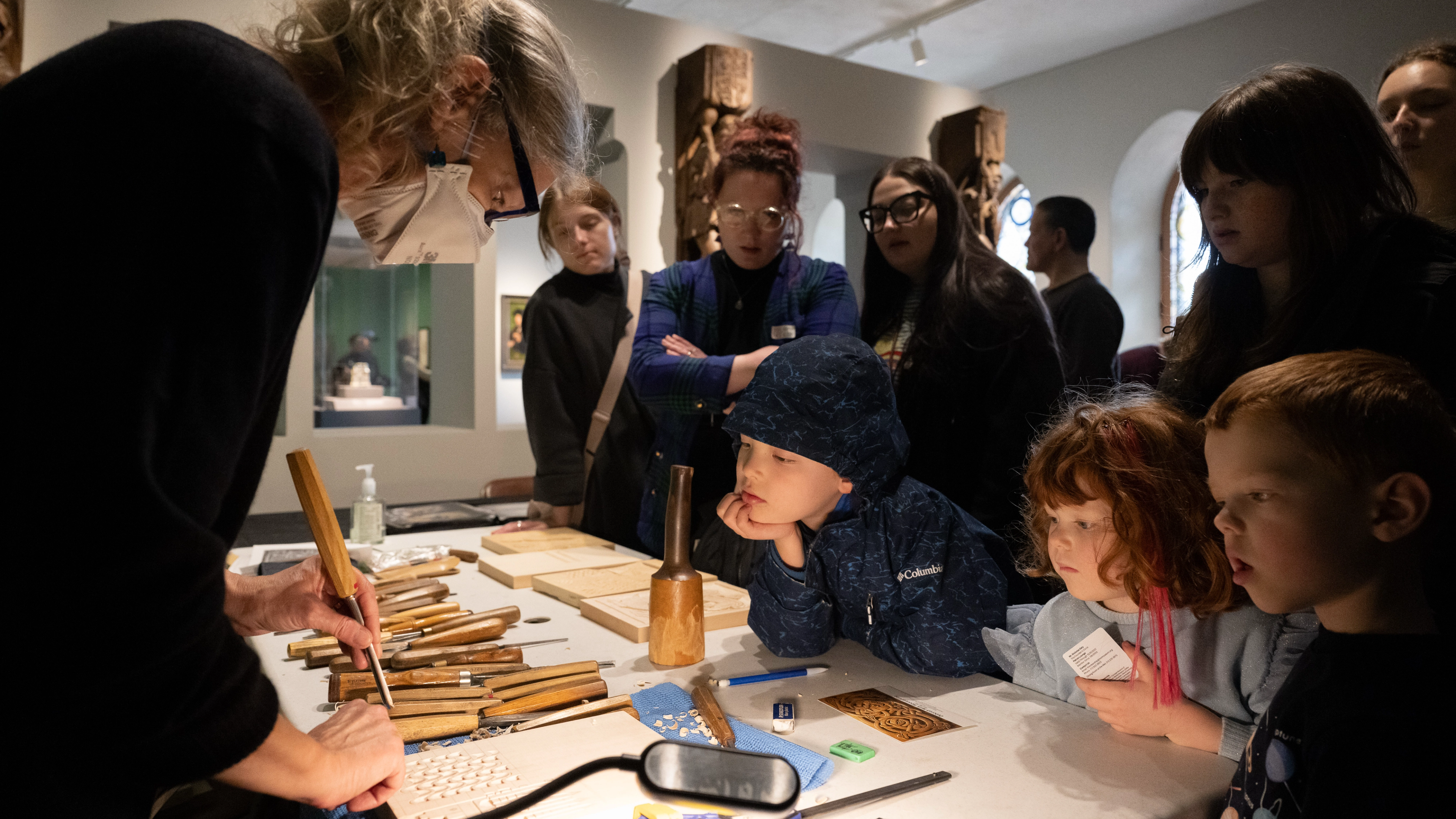 A group of students gather around a metalwork artist. 