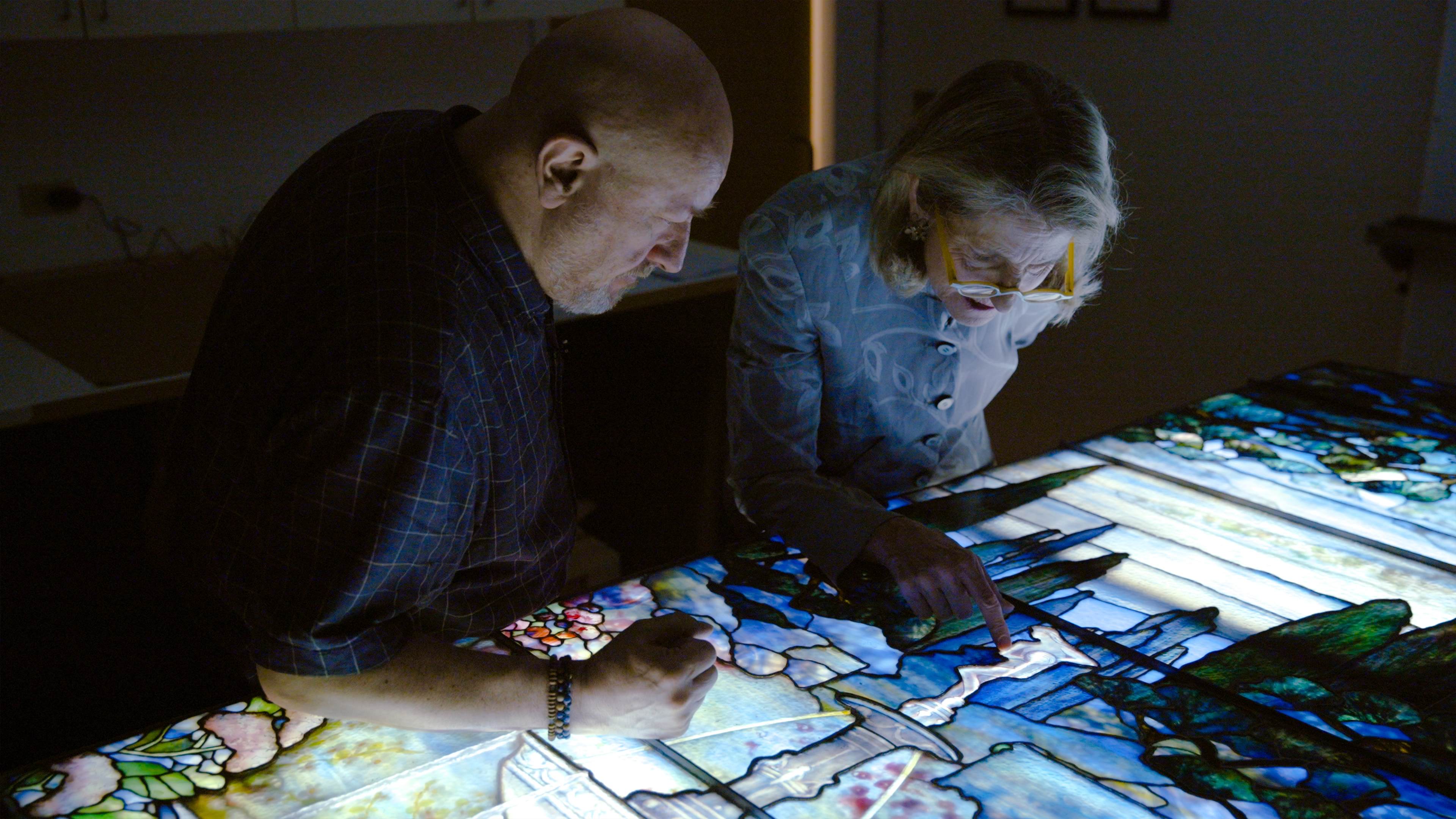 Two people look closely to inspect at the Tiffany Window. 