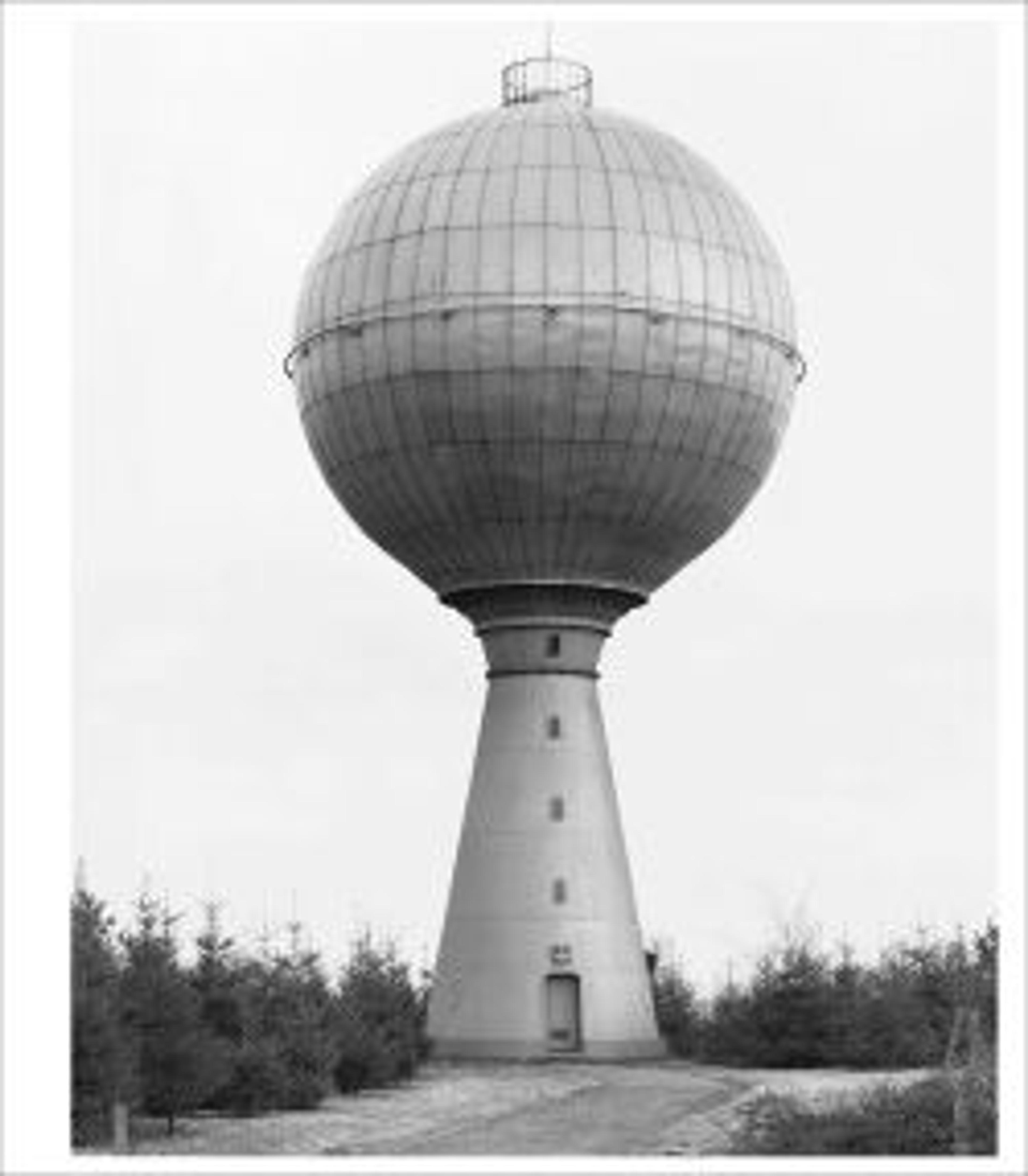 a black and white photograph of a spherical water tower with a forest in the background