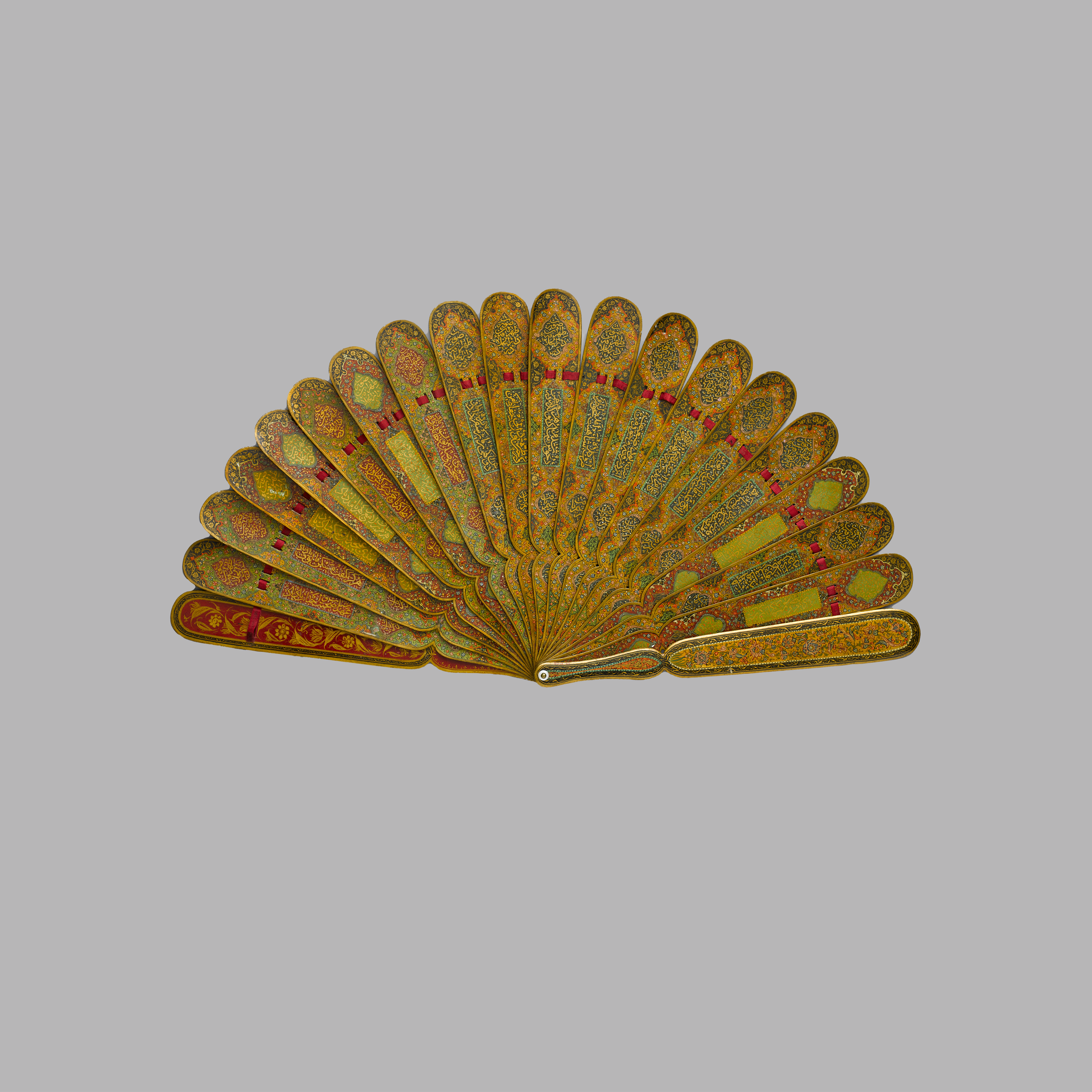 Ornate folding fan with golden patterns and red accents on each rib, intricately designed with floral motifs, displayed against a neutral background.