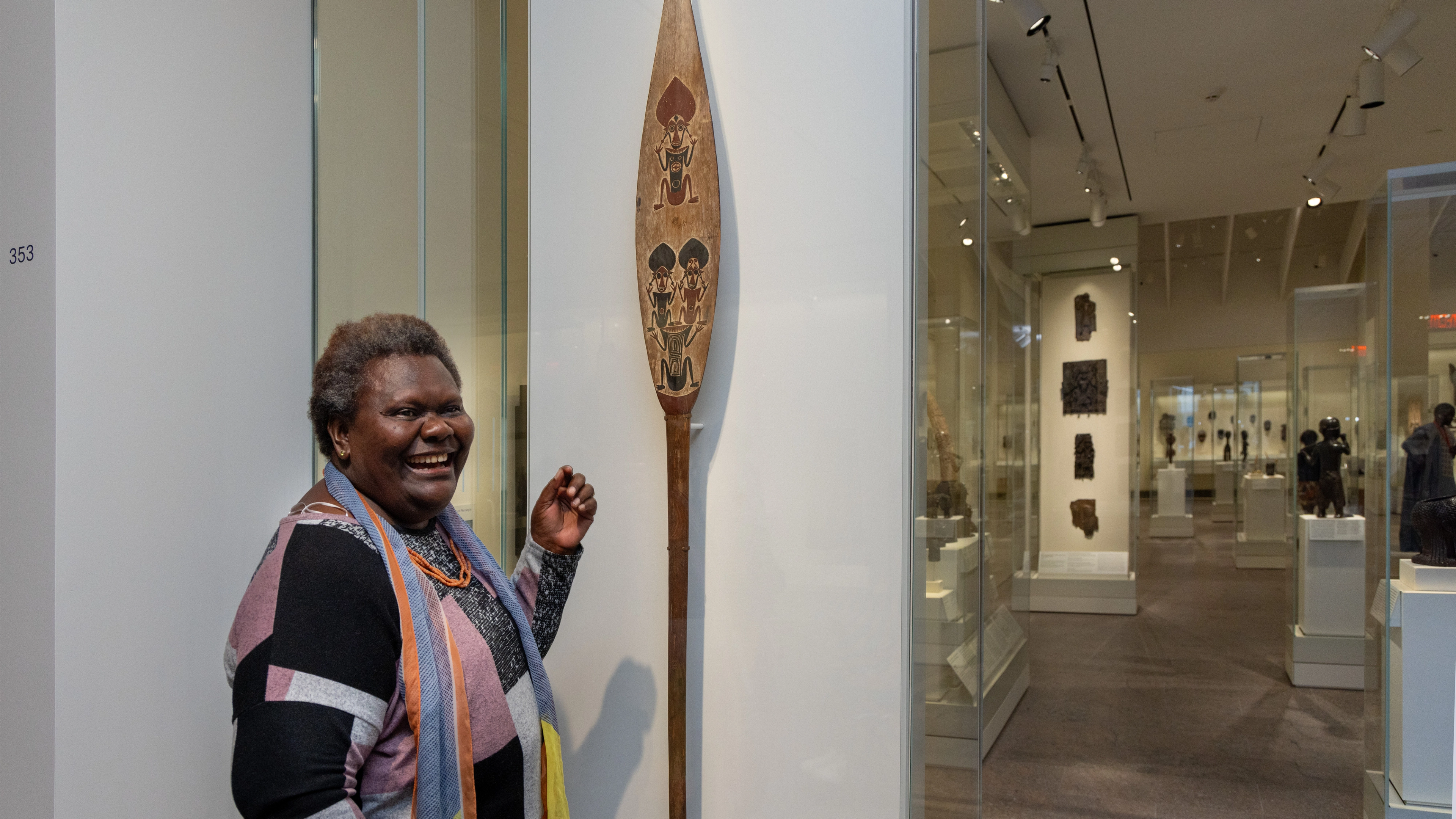 Sana Balai standing in front of a ceremonial paddle in the Oceania galleries at The Met.
