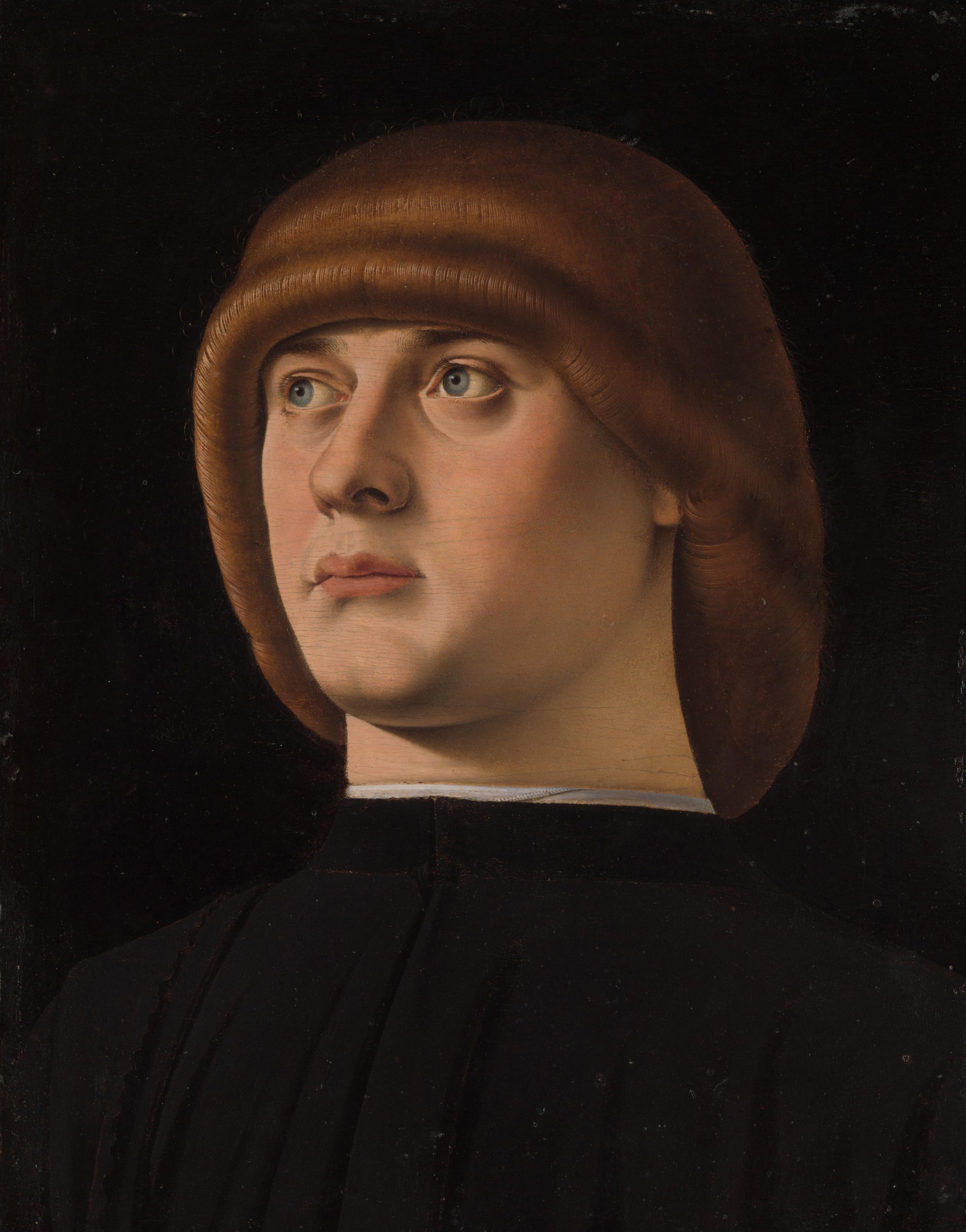 Portrait of a carefully groomed young man clad in black against a black background.