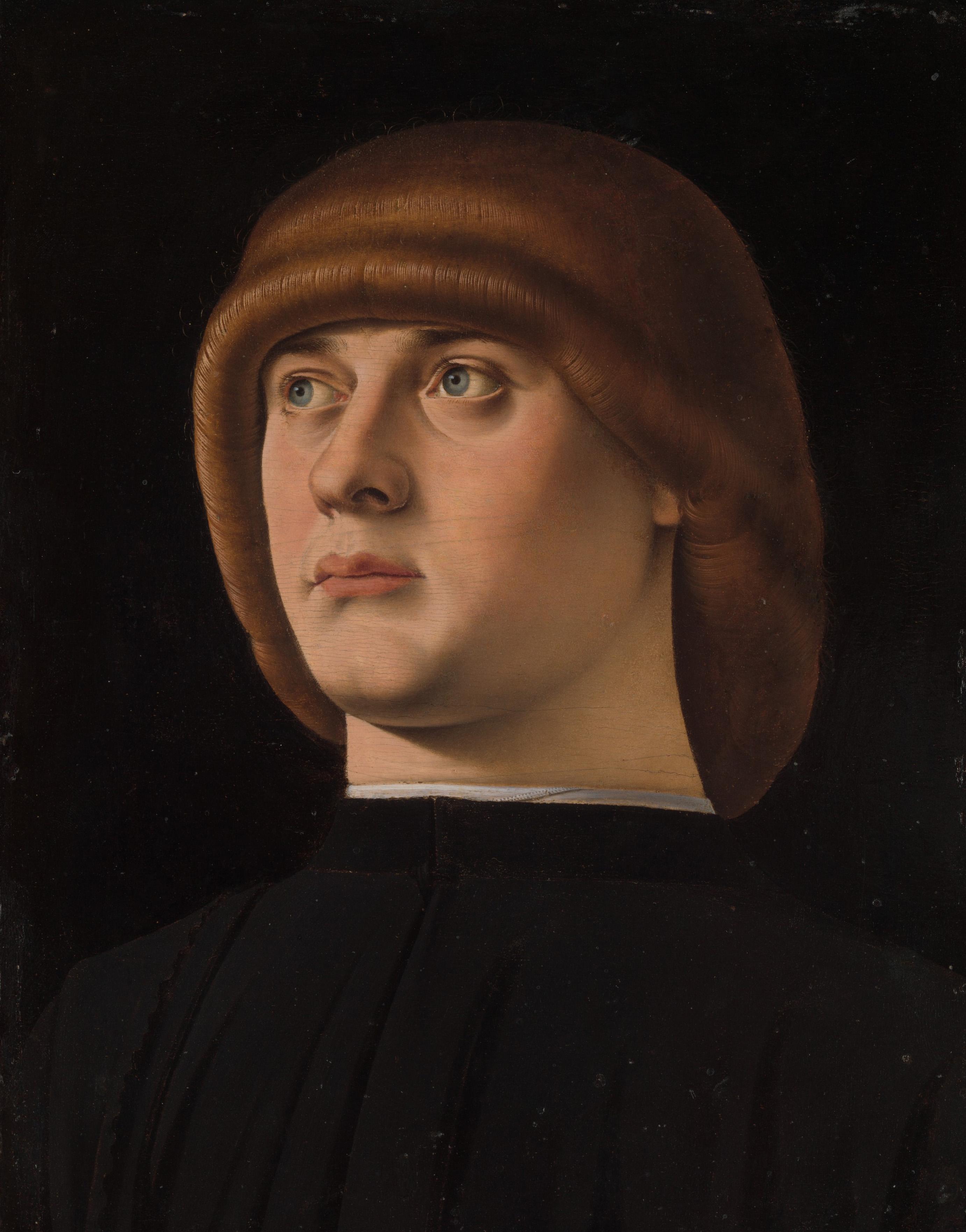 Portrait of a carefully groomed young man clad in black against a black background.