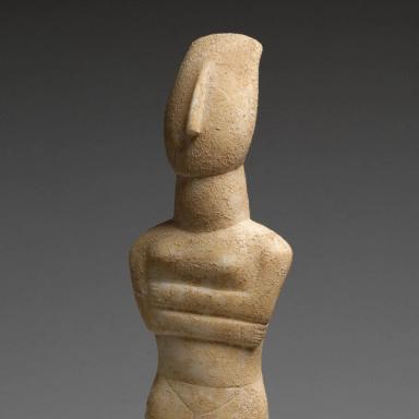 Nude stone Cycladic figure with it's arms crossed against a grey background.