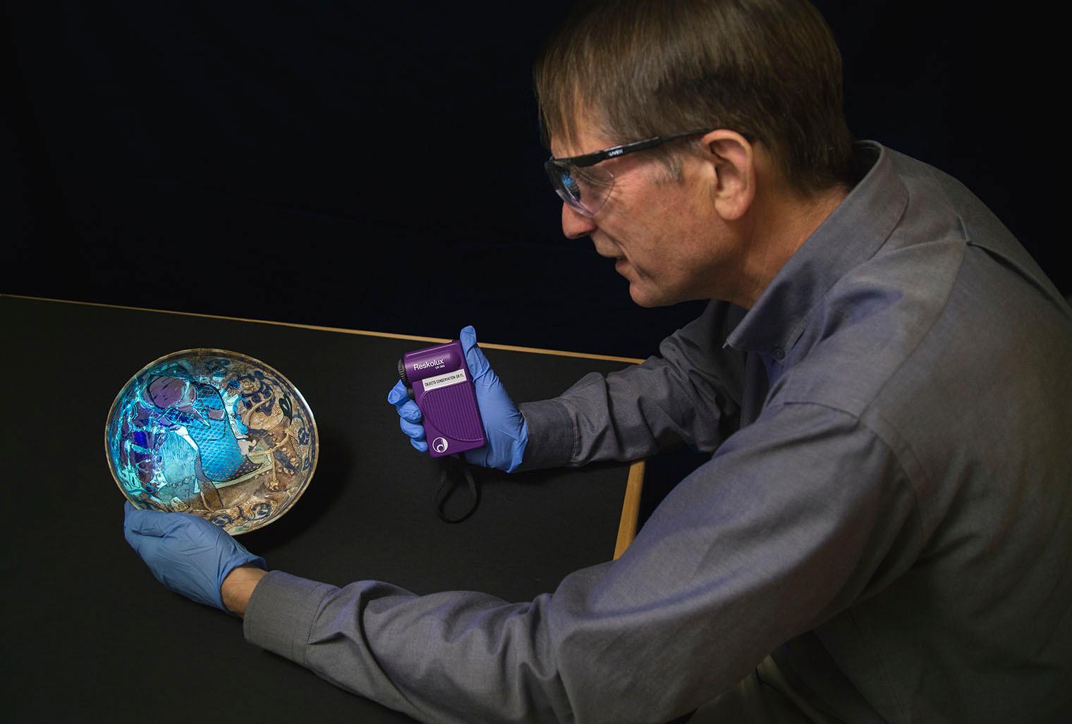 Conservator examining a ceramic dish using ultraviolet radiation.