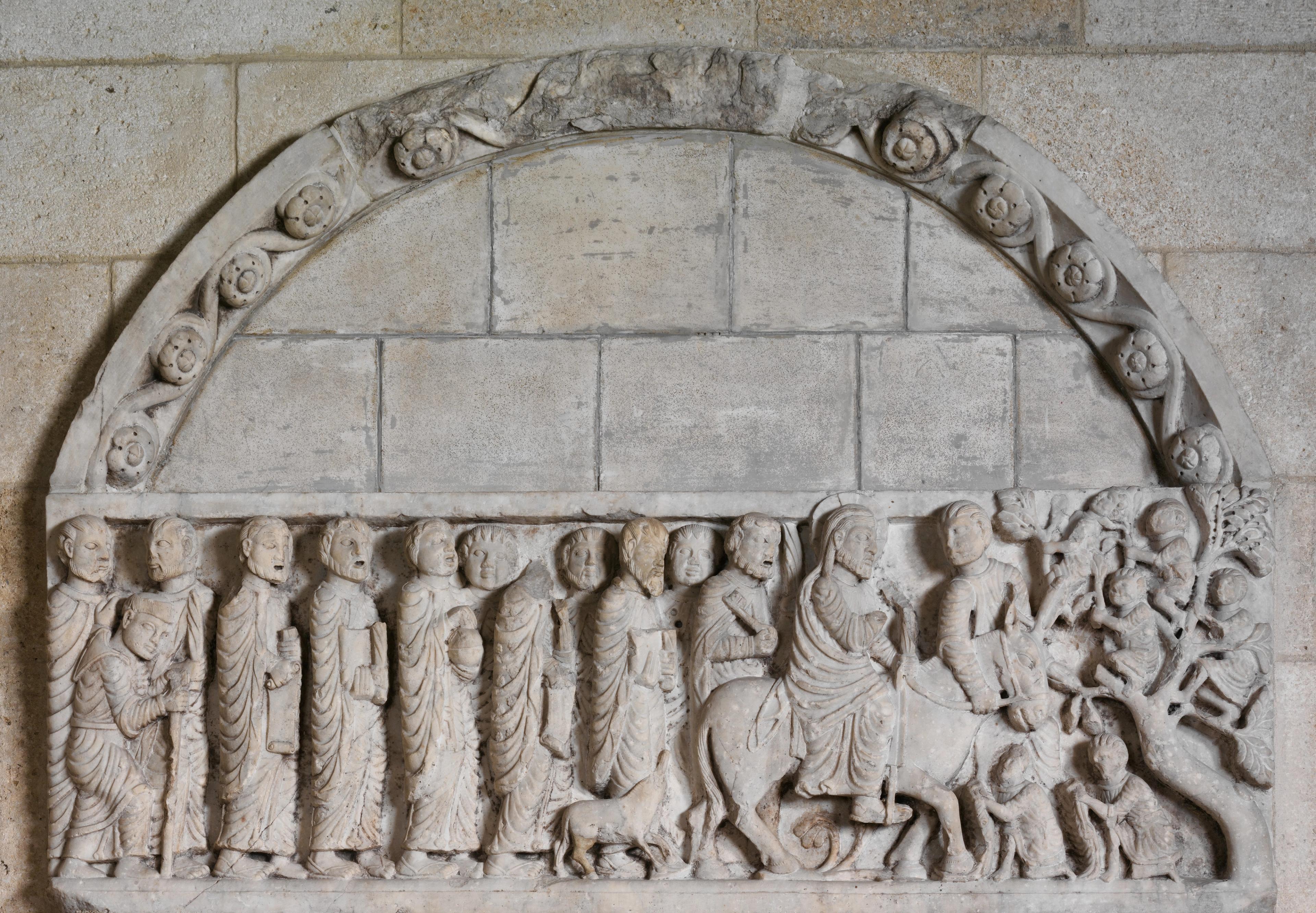 Detail of a stone arch, showing a procession of figures, including Jesus, as he entered Bethlehem.