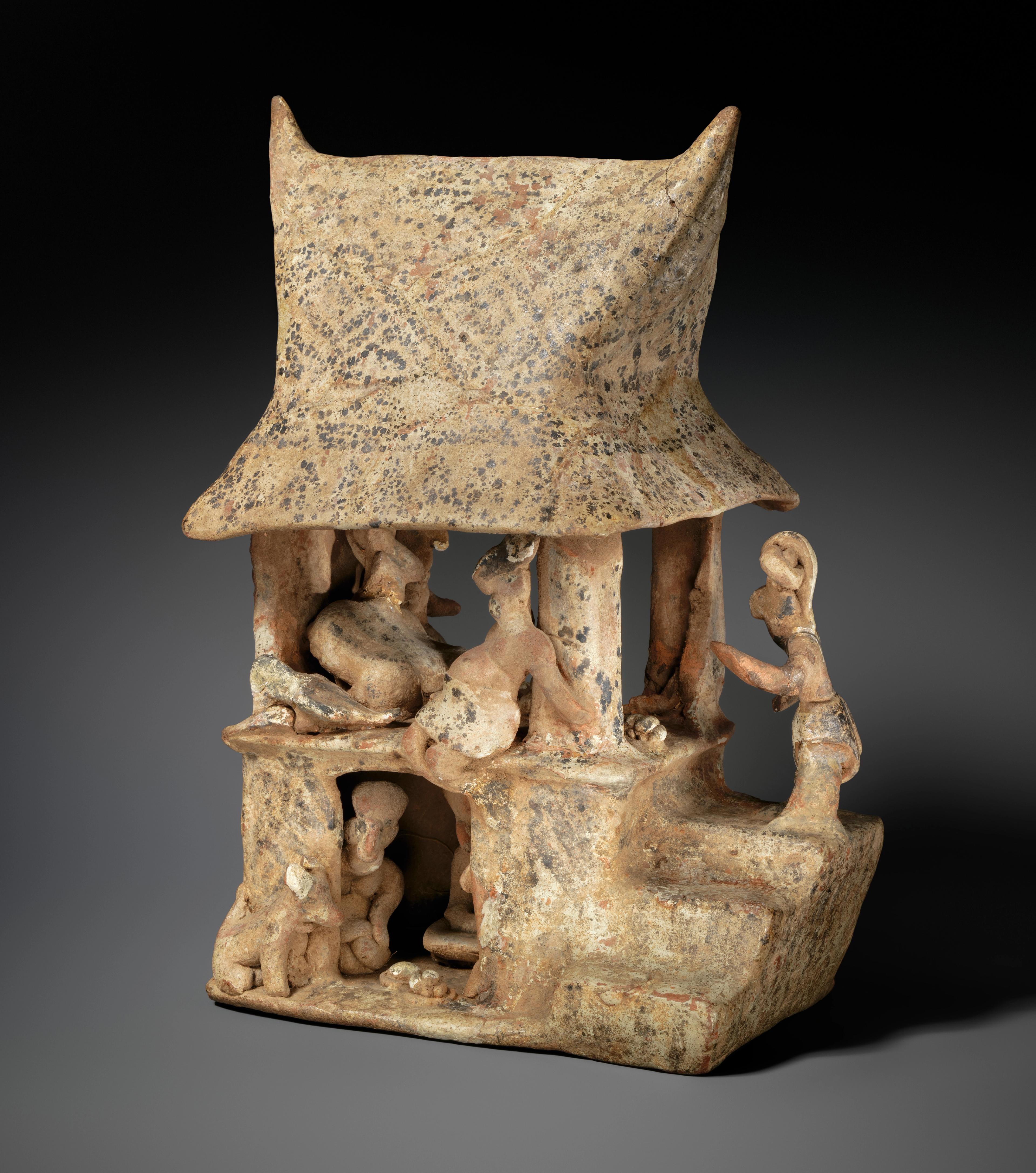 Open-air model of a home with several figures engaged in housework.