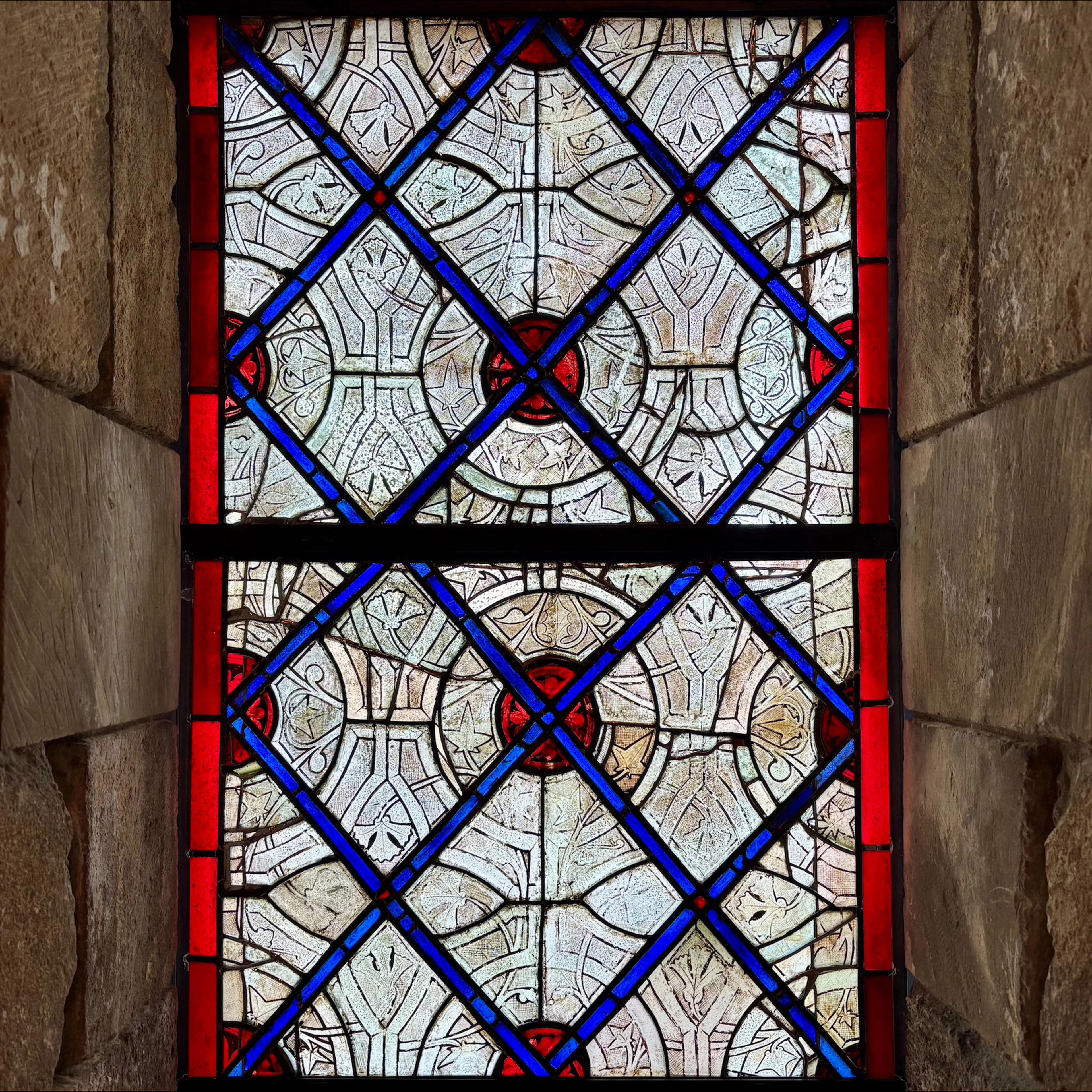 A blue and red stained-glass window nestled between rectangular stones.