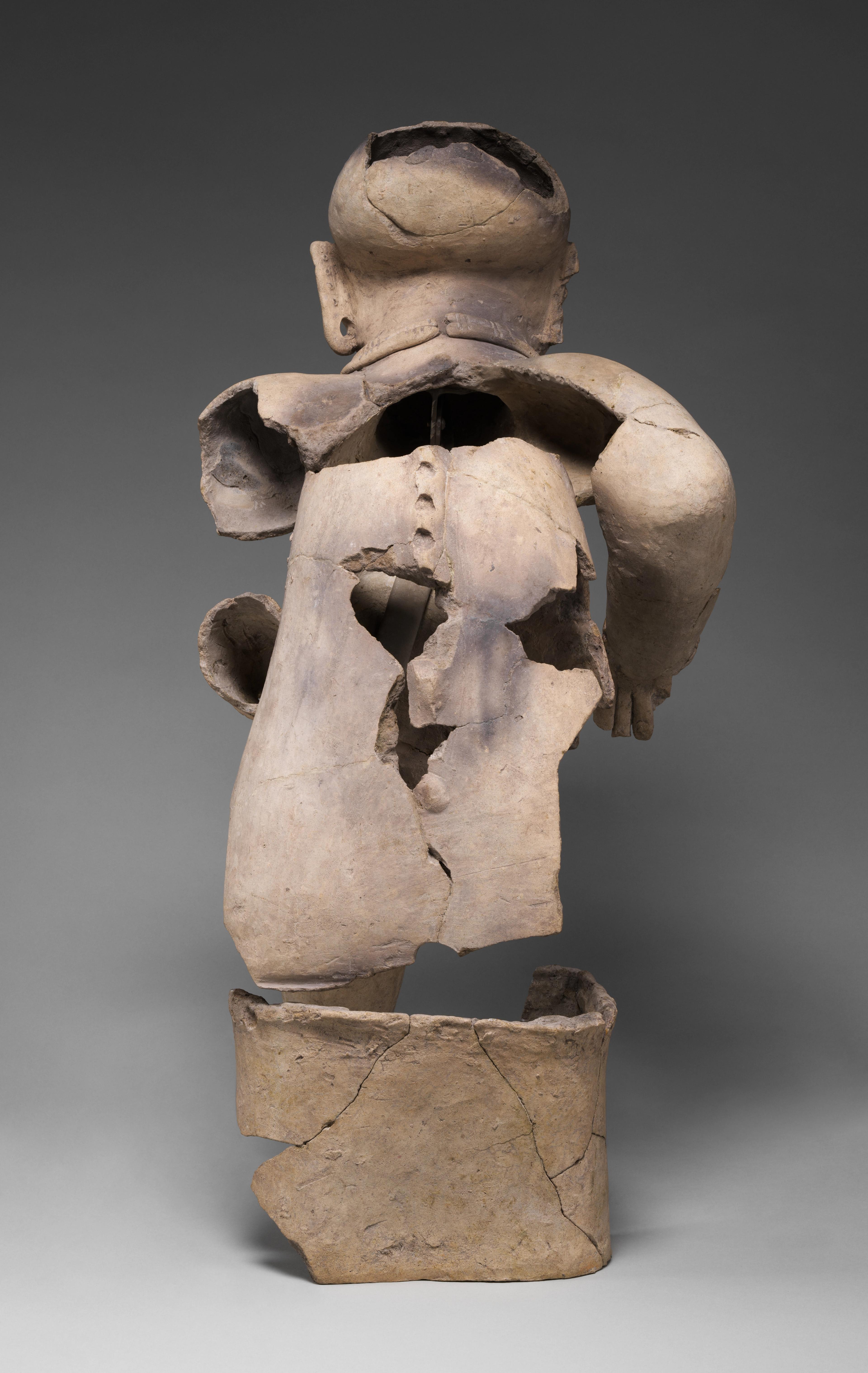 The back of a seated elder statue with a marked spine resembling iguana spikes.