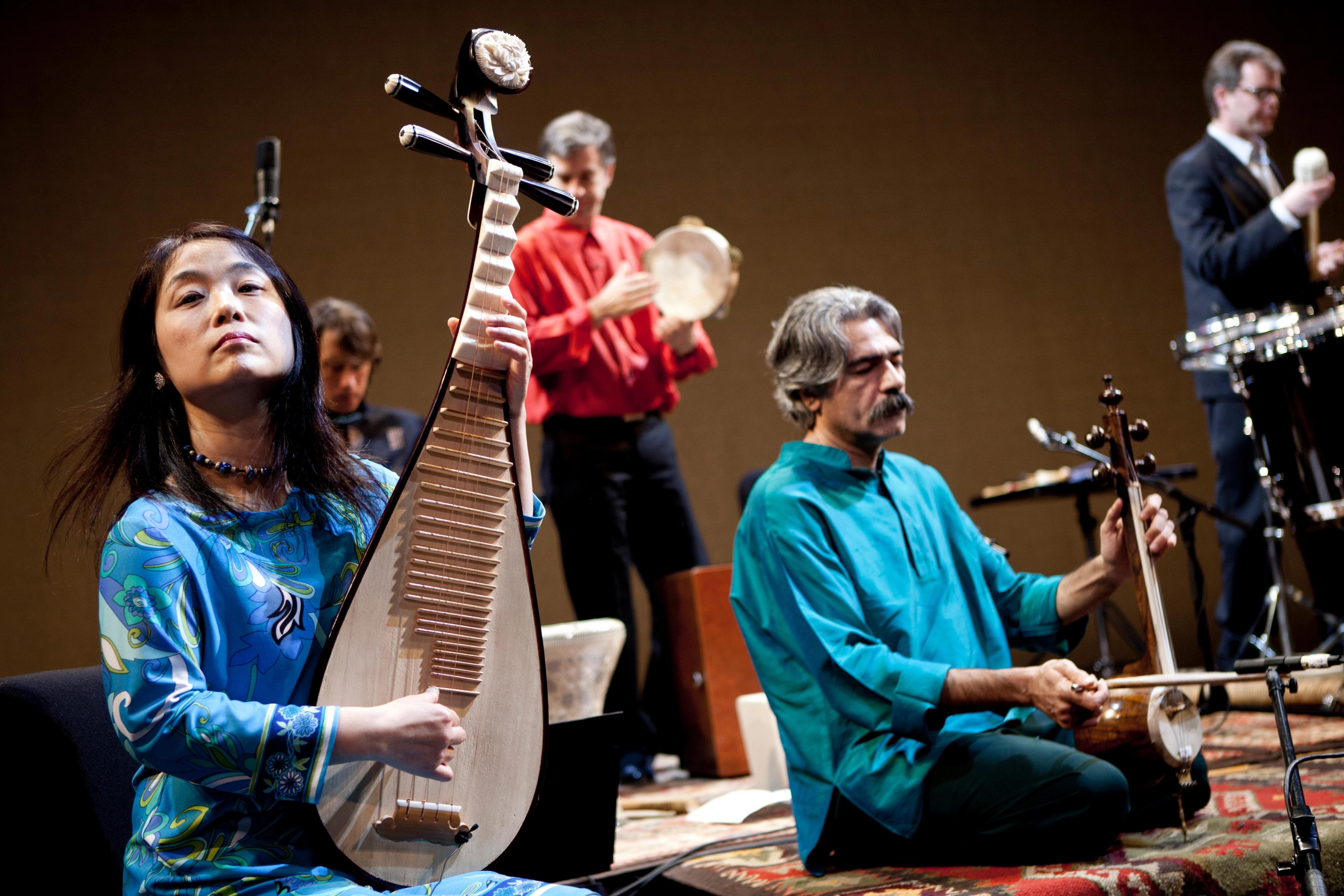 Wu Man dynamically playing the pipa on stage with four other musicians.