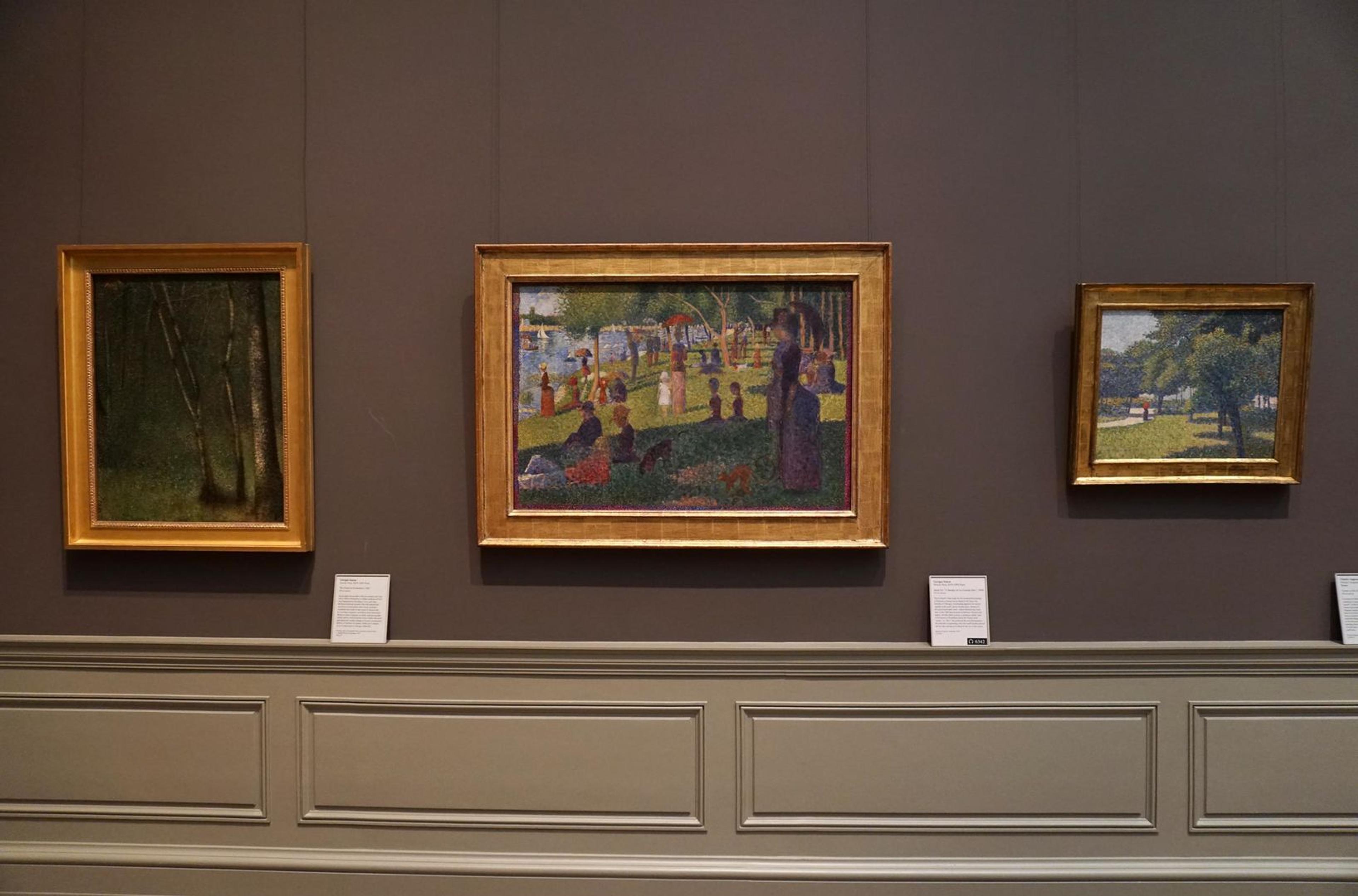 View of three paintings in a gallery, two by Seurat and one by Charles Angrand