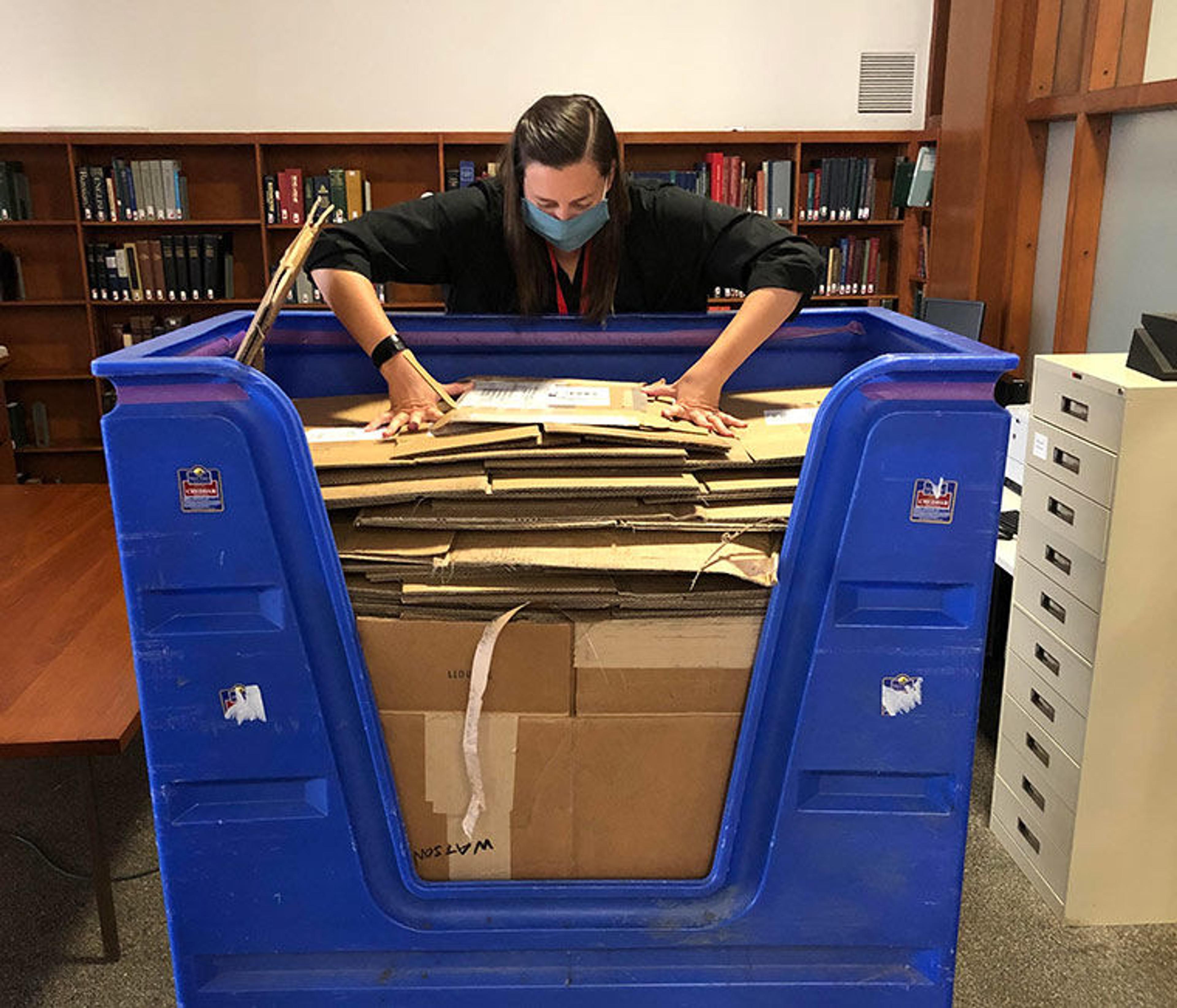 A librarian stuffing a blue recycling bin full of broken down boxes