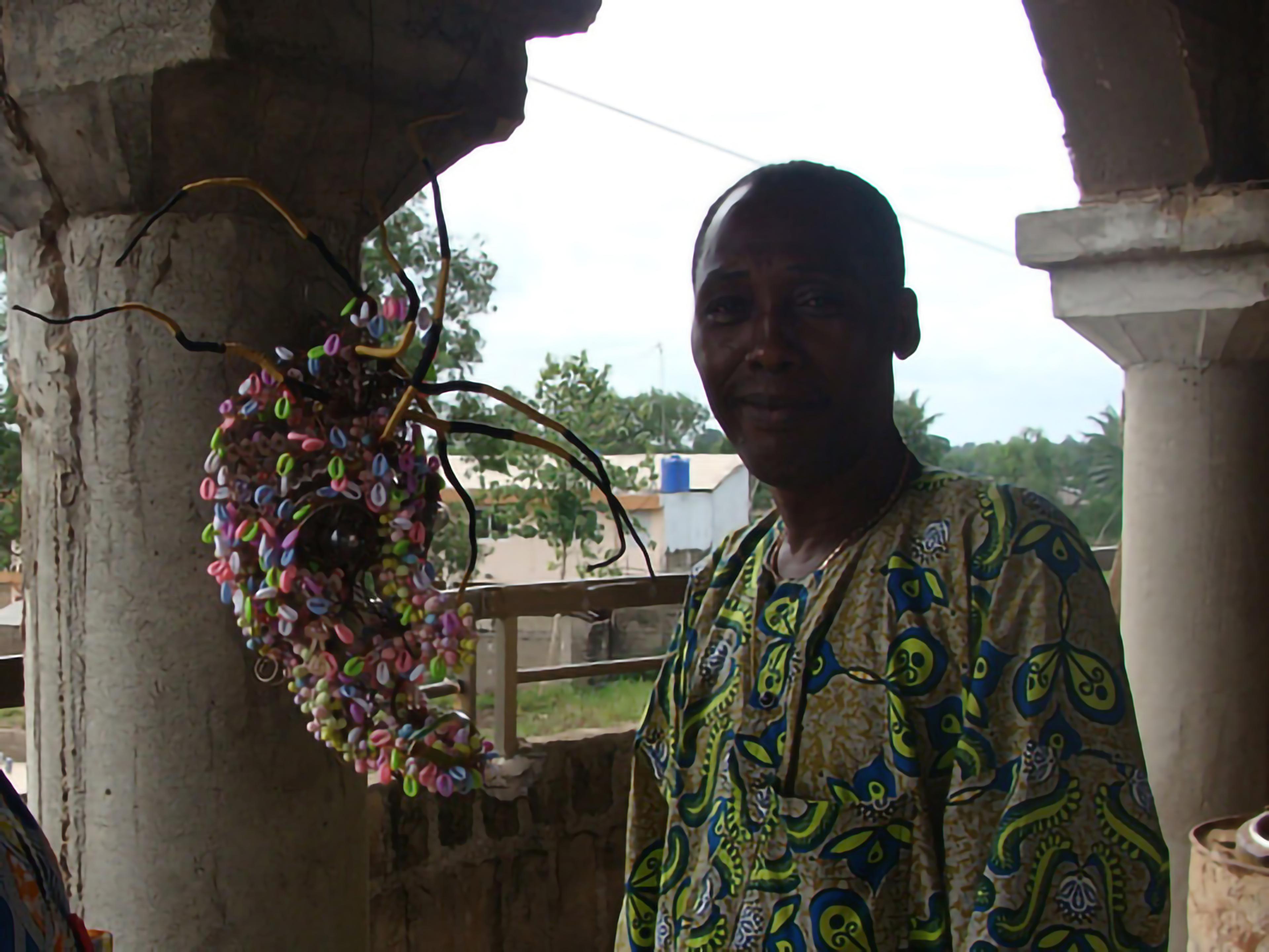 Photo of the artist Calixte Dakpogan posing next to a multicolored mask