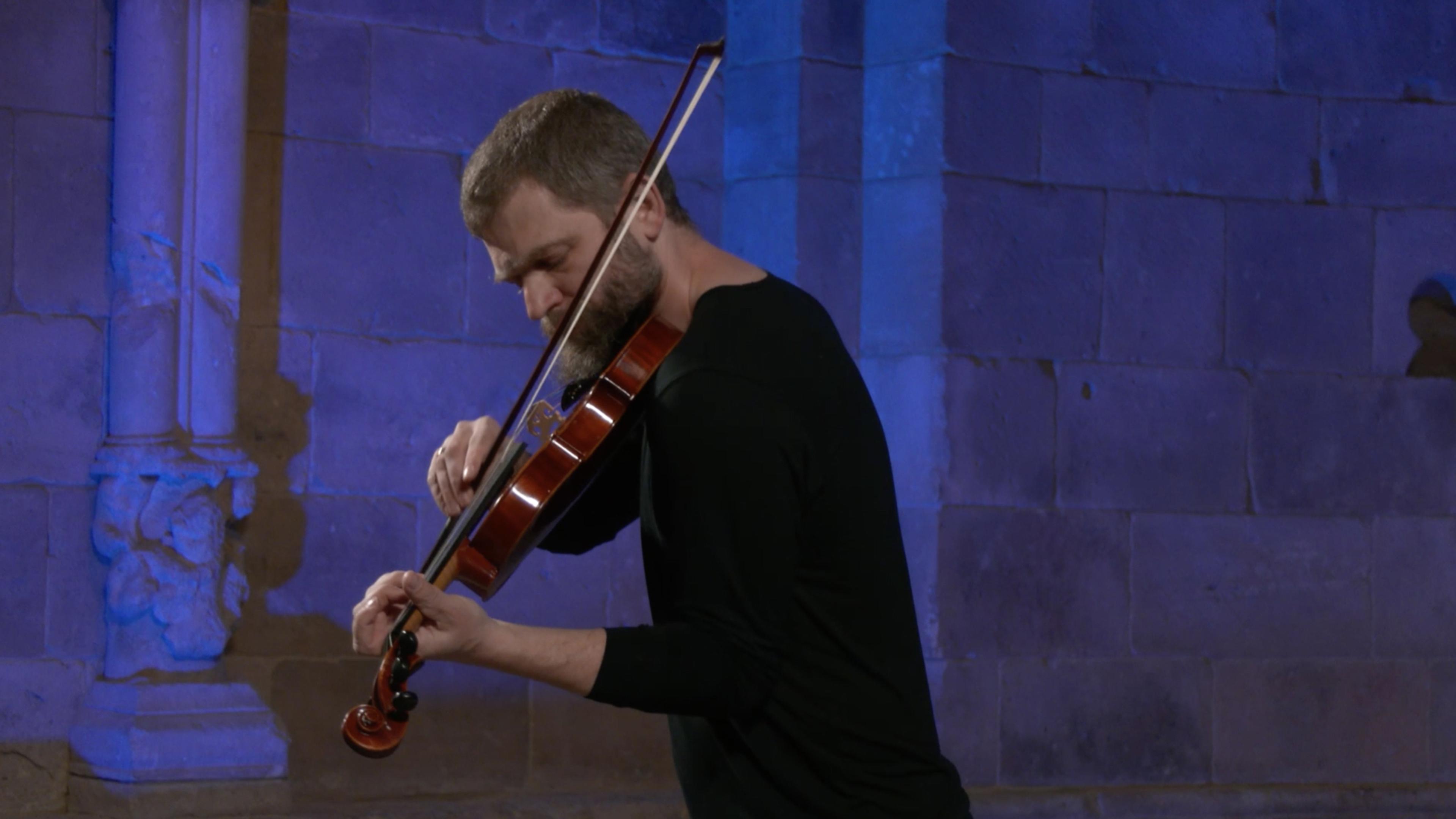 Johnny Gandelsman playing the violin against a blue lit background.