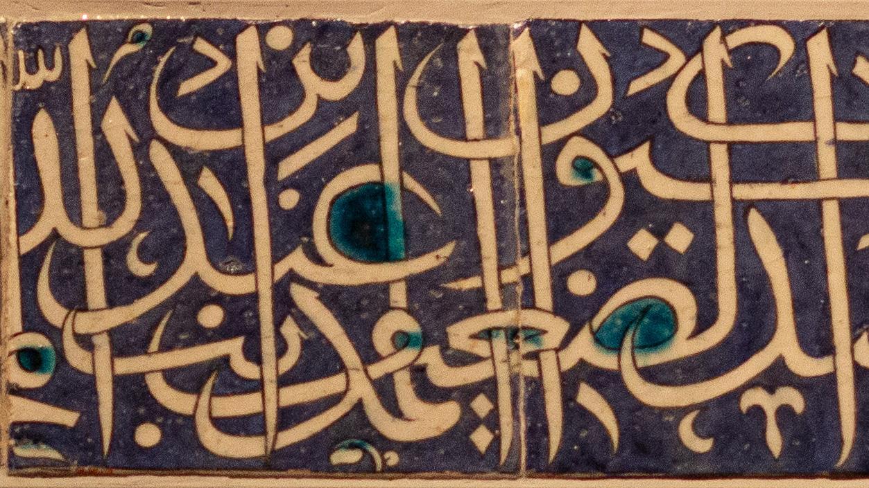 Ceramic tile panel with light-colored calligraphy against a darker background.
