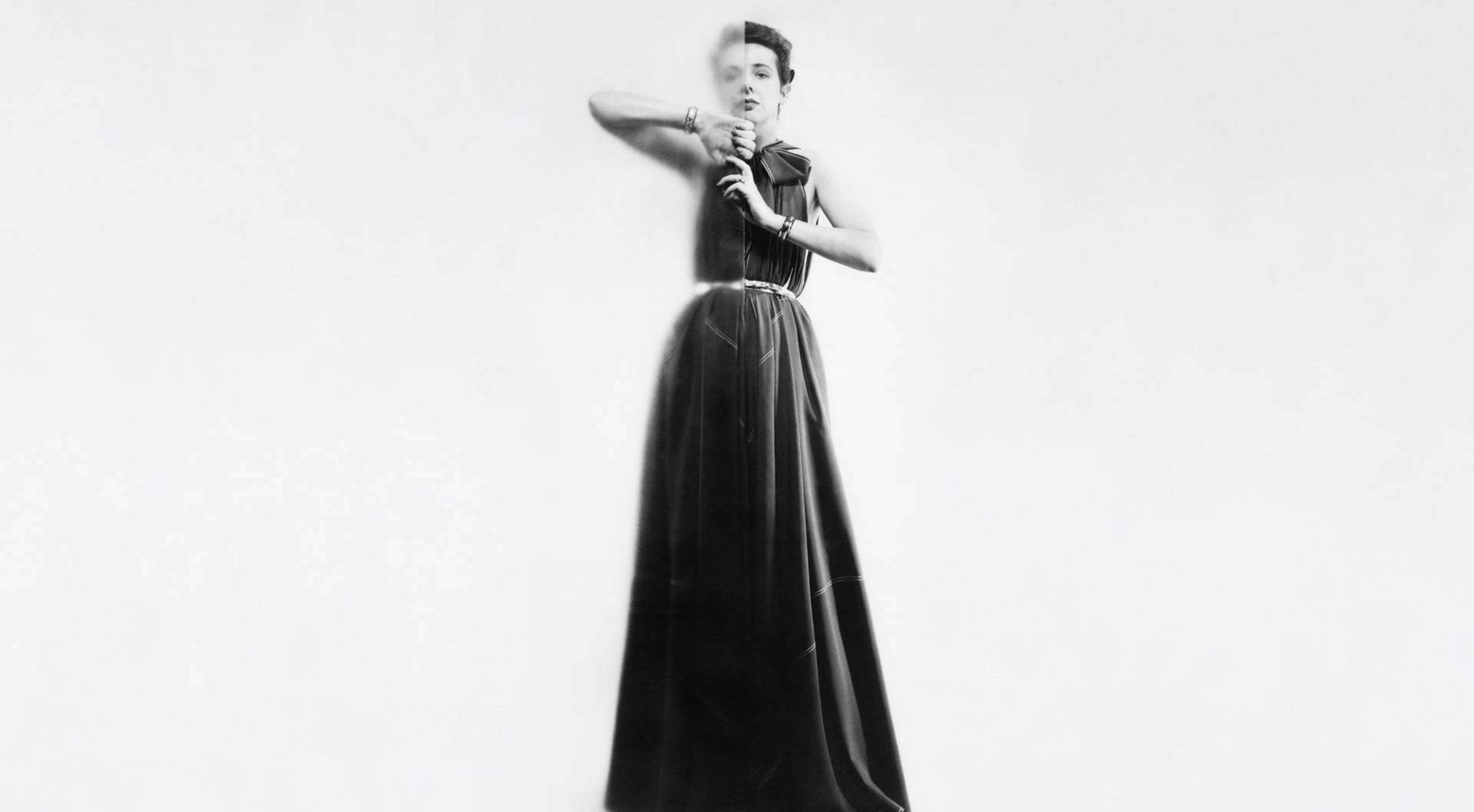A black and white photograph of a light-skin-toned woman wearing a long, dark evening dress.