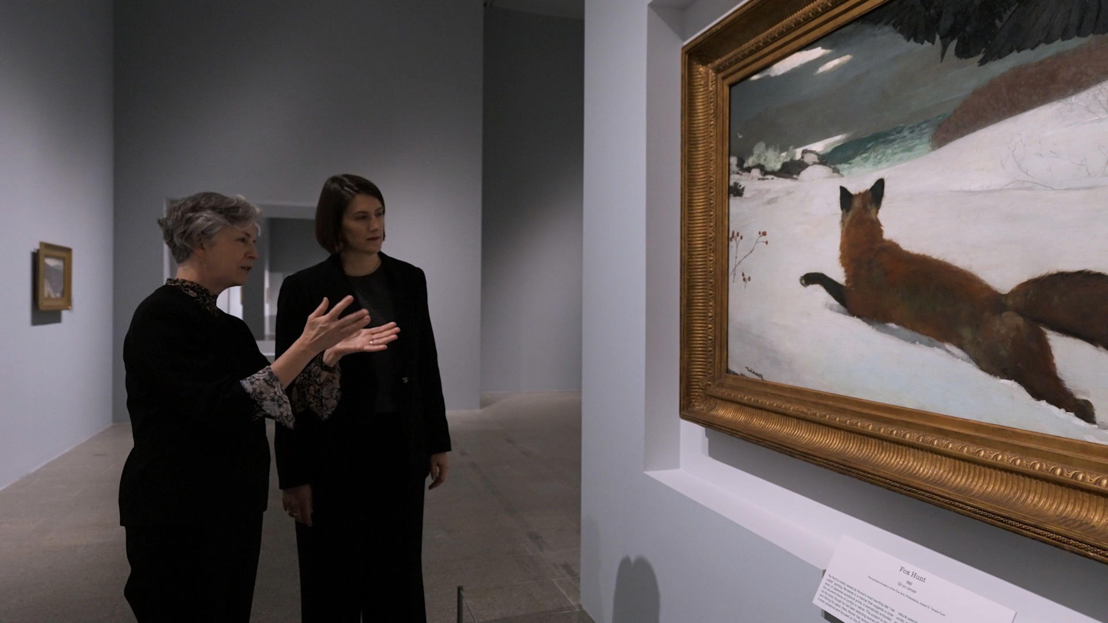 Two female curators standing in front of Winslow Homer's painting Fox Hunt. 