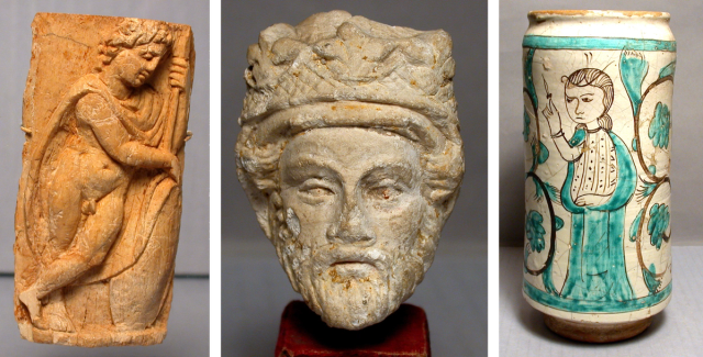 At left, a bone panel showing a partially nude warrior leaning in repose. At center, the stone head of a man with a beard and crown. At right, a jar showing a woman holding a leaf.