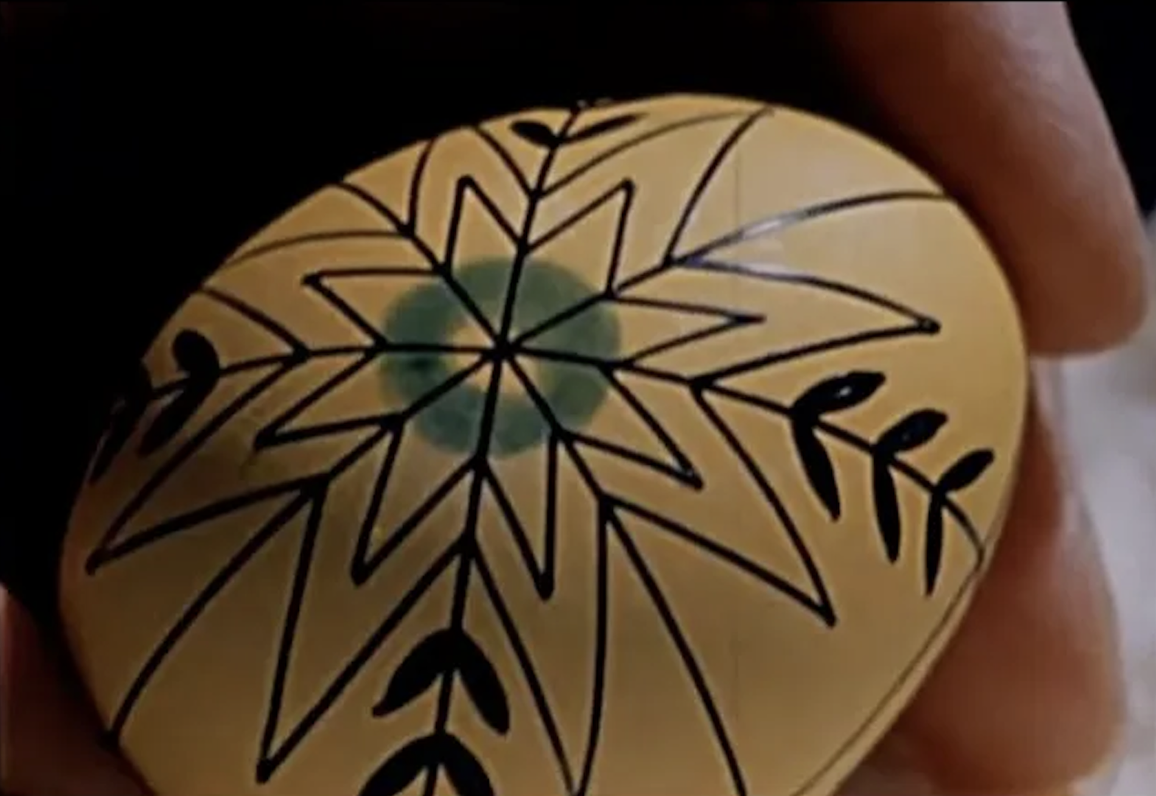A yellow egg painted with an elaborate design is held as it is decorated.